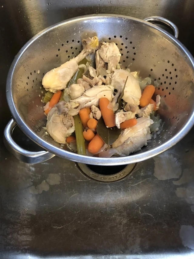 Cooked chicken and vegetables in in a strainer that&#x27;s sitting in the sink