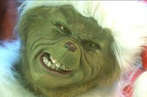 Jim Carrey as the Grinch wears a Santa hat and grinds his teeth together, brows furrowed