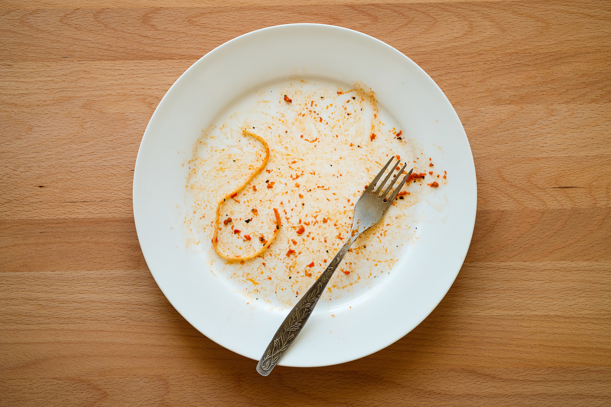 An empty plate with remnants of a red sauce and spaghetti