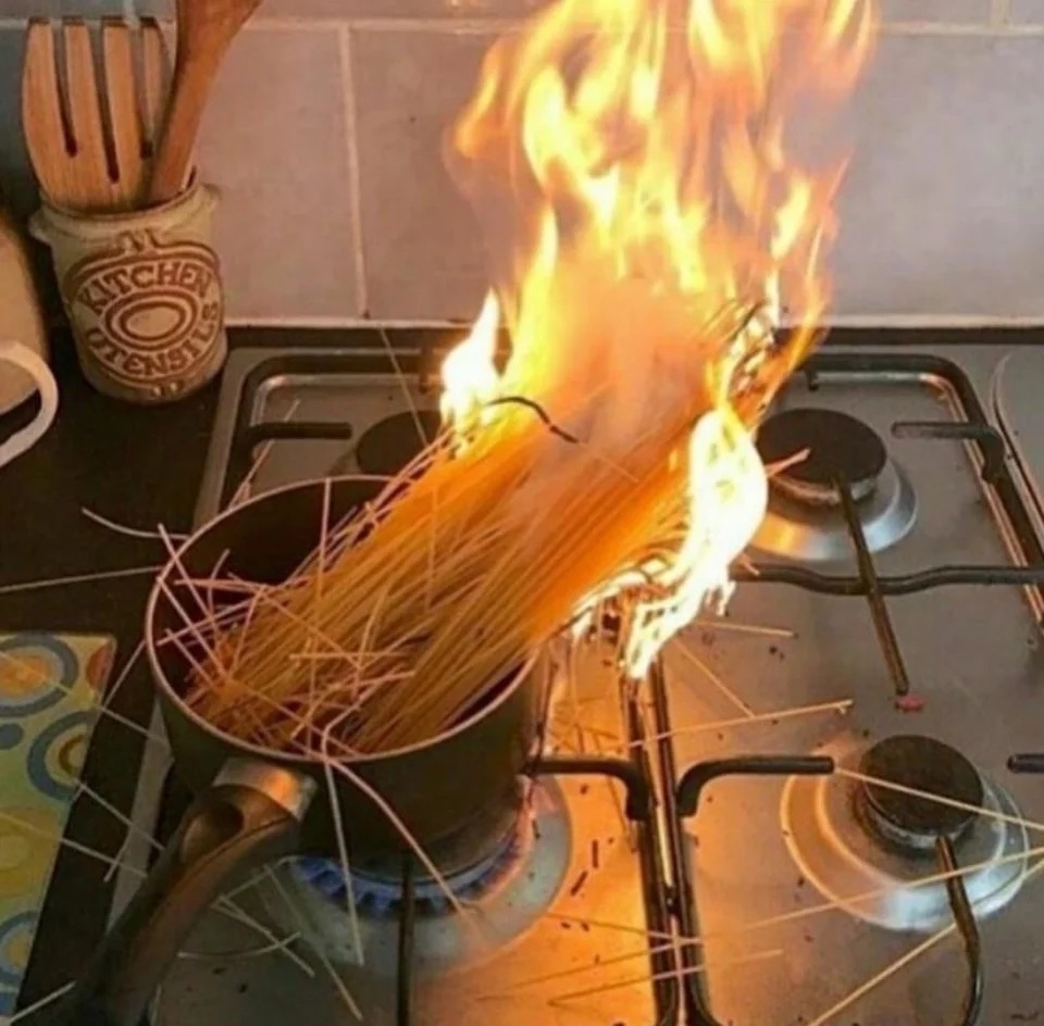 Uncooked strands of spaghetti on fire in a small pot on the stove
