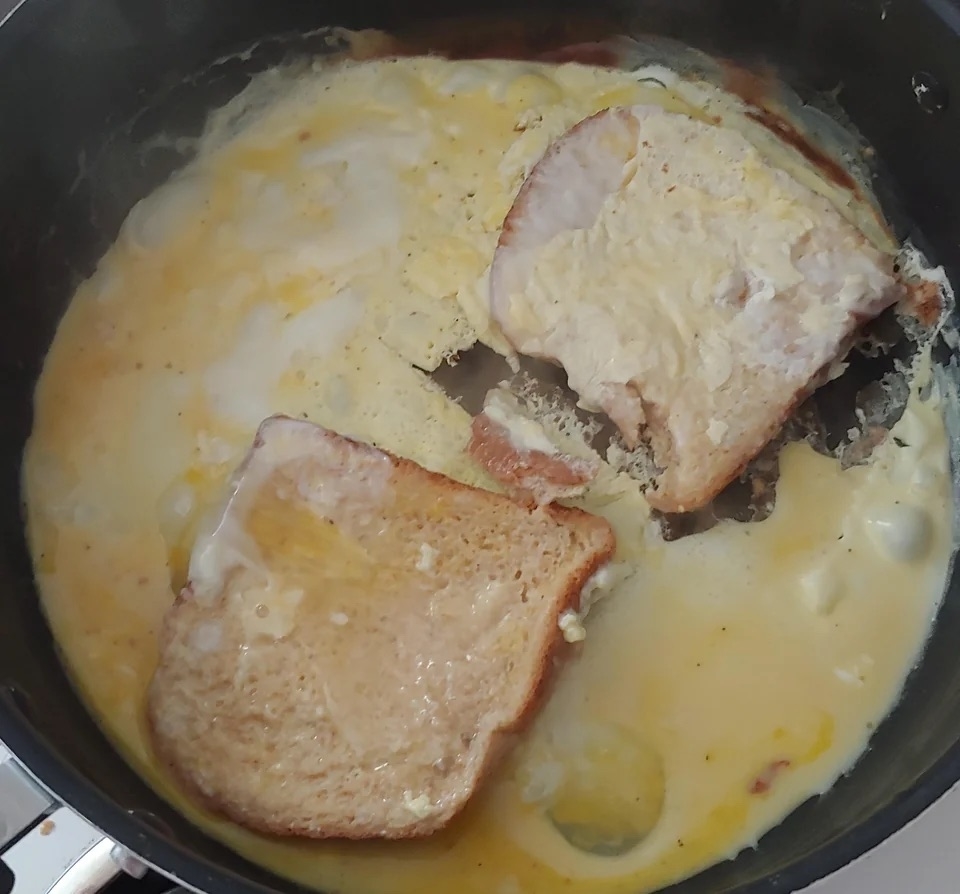 Two pieces of bread in a pan surrounded by a flat, cooked egg mixture