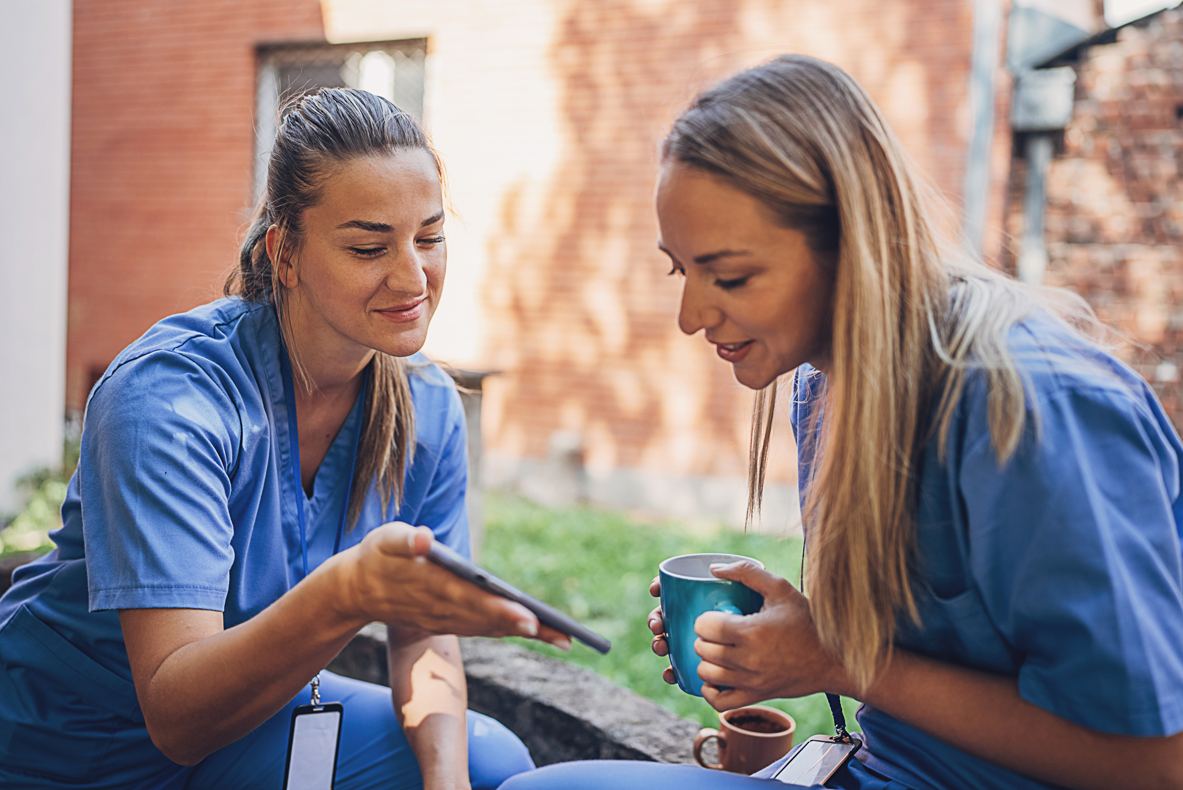 Two people wearing hospital scrubs gossiping on their break