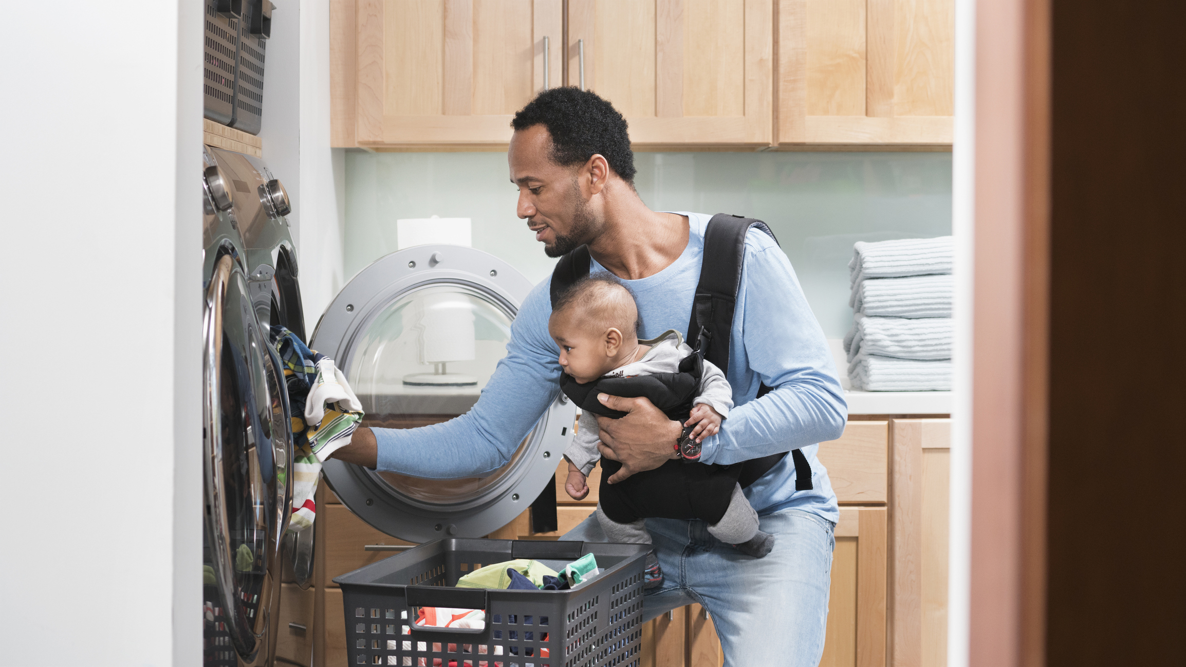 A father holding his child in a baby carrier while he does laundry