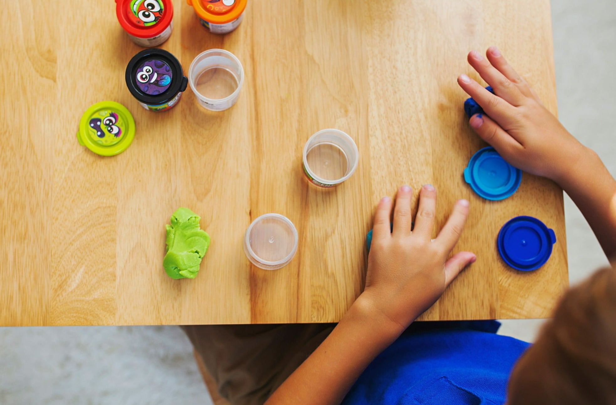 A kid playing with four small tubs of scented dough