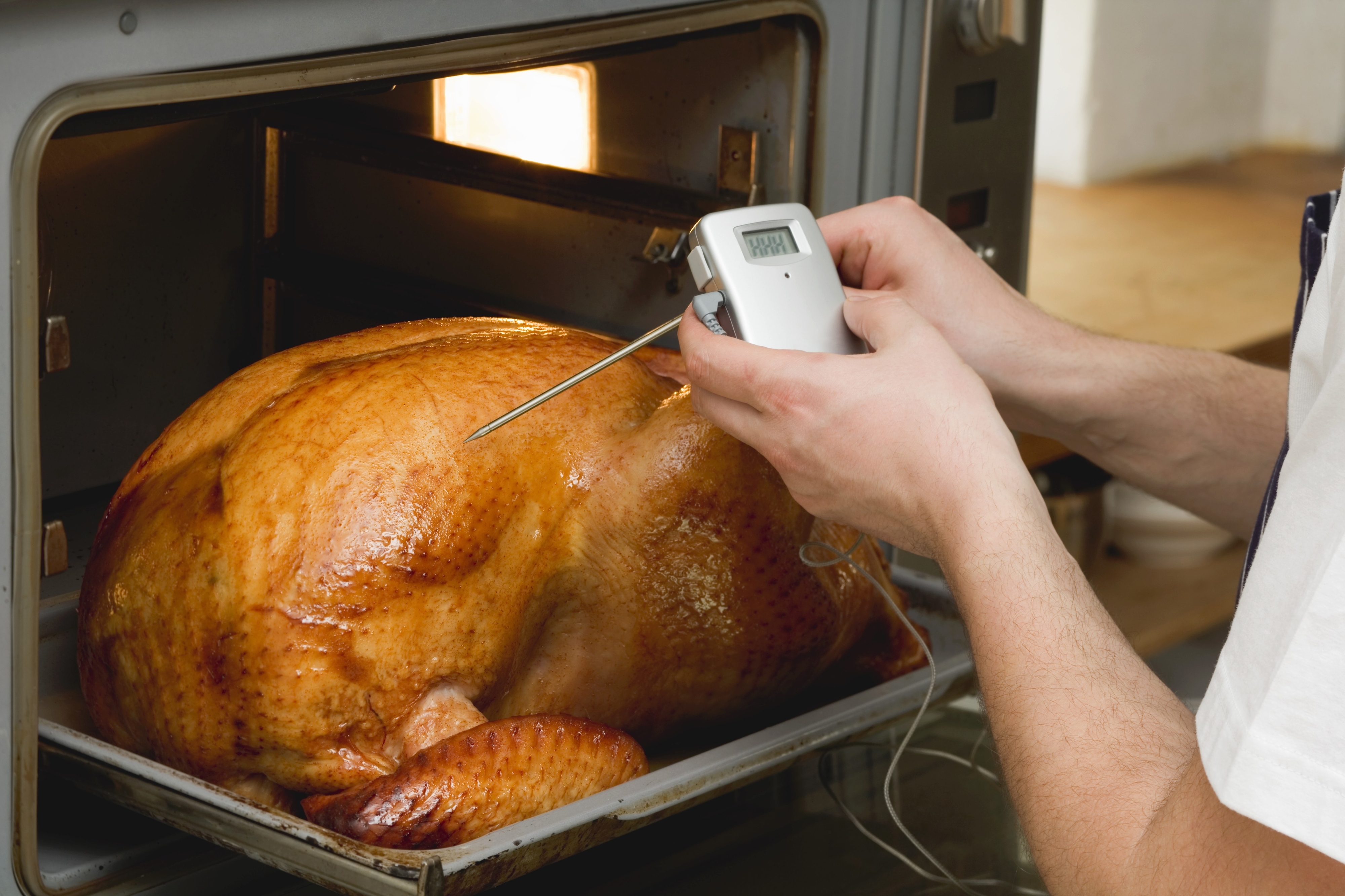 inserting a meat thermometer into the breast of a roasted turkey
