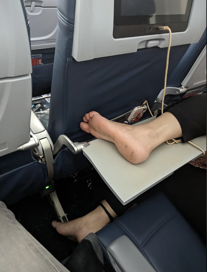 a person&#x27;s feet on someone&#x27;s tray table in a plane