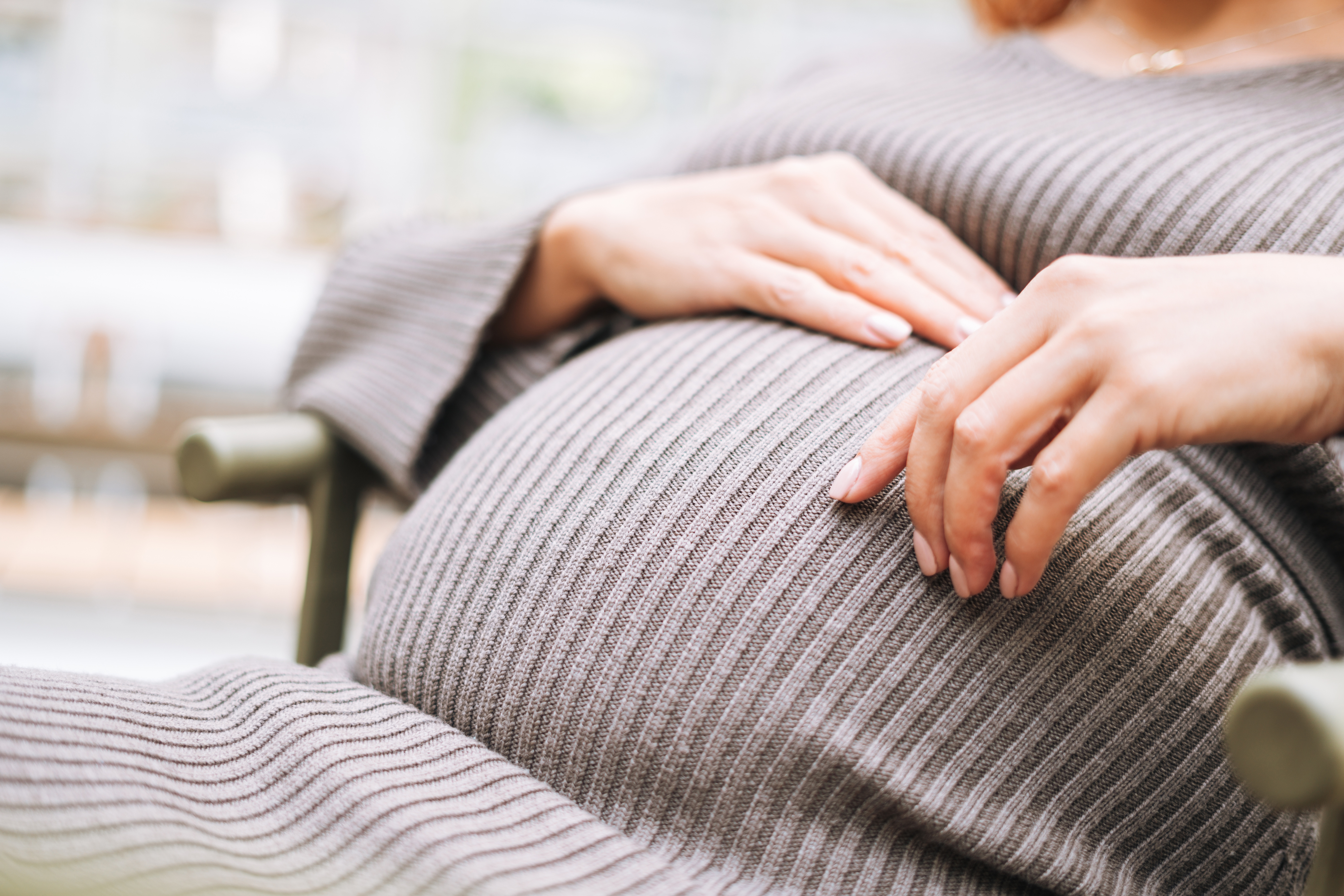 a shot of a pregnant woman's belly while she rest her hands on top of it