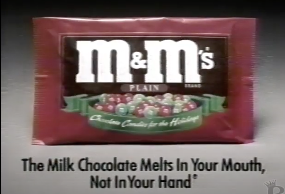 Screenshot from M&amp;amp;M&#x27;s commercial, with a bag of the holiday M&amp;amp;M&#x27;s and text, &quot;The Milk Chocolate Melts in Your Mouth, Not in Your Hand&quot;
