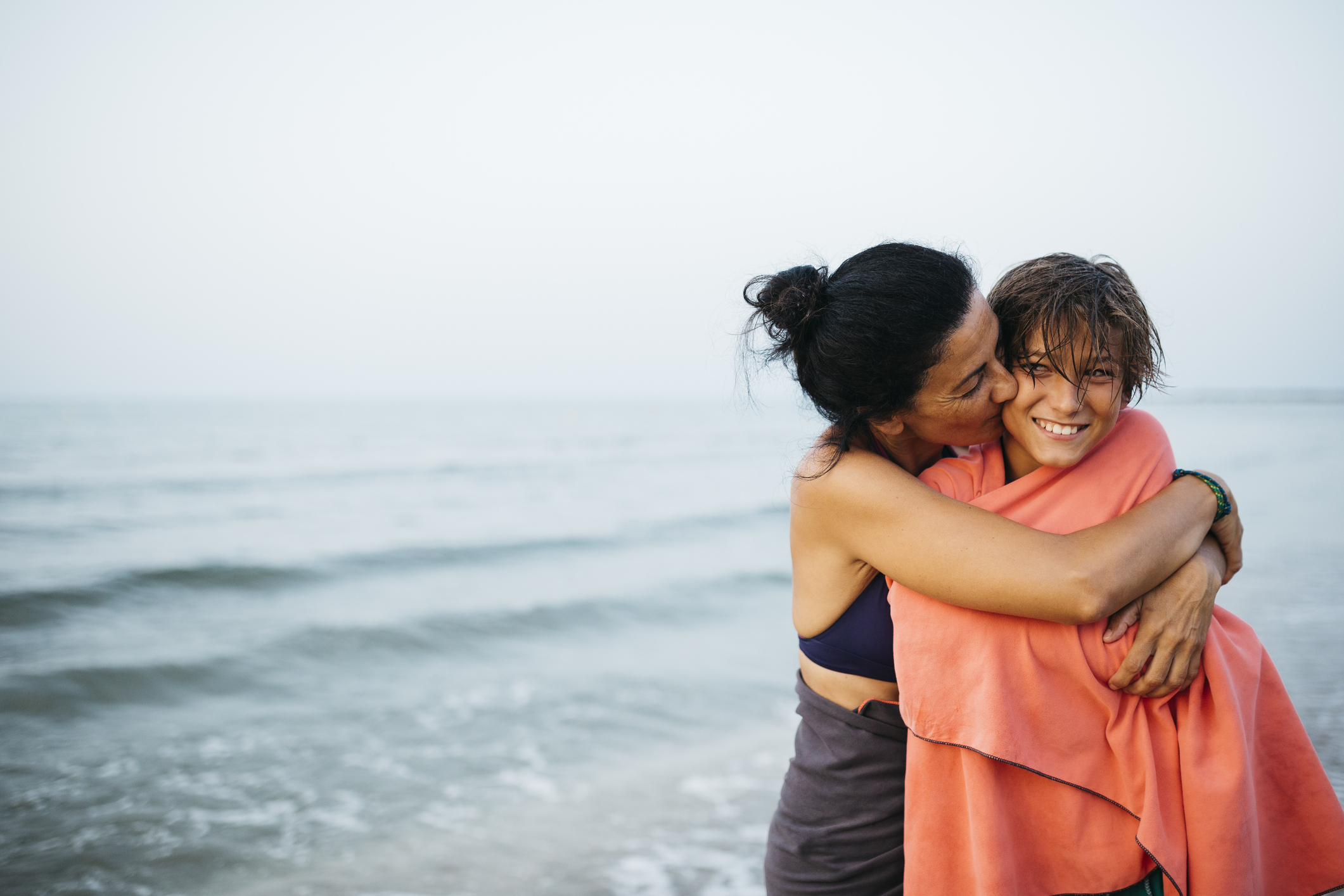 A mom is hugging her son at the beach