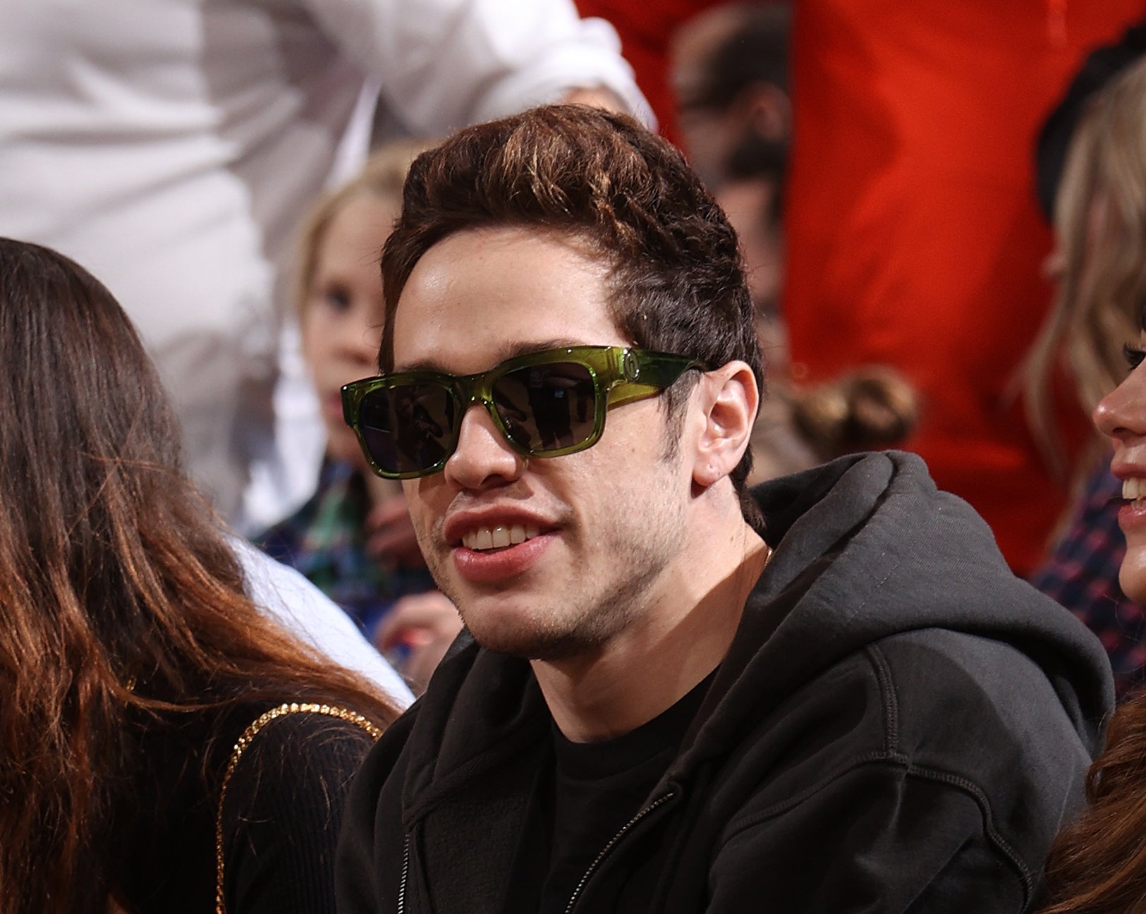 he's sitting down wearing sunglasses with grown-out hair