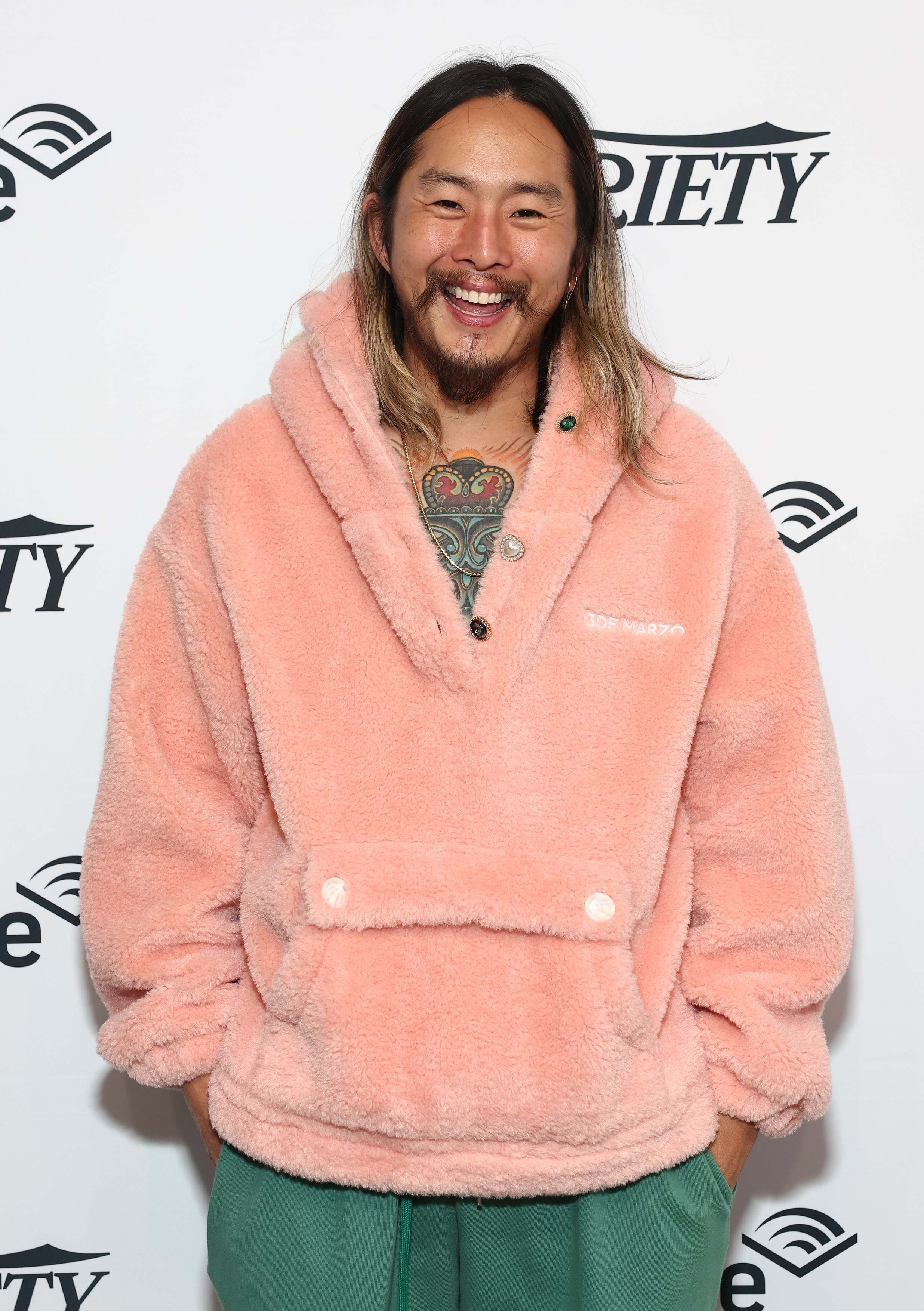 closeup of him in a fuzzy sweater, smiling big with long hair at an event