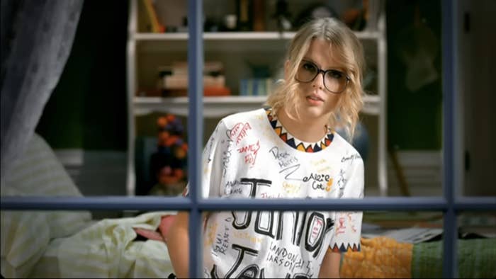 Taylor in the T-shirt looking through her bedroom window in a scene from the music video
