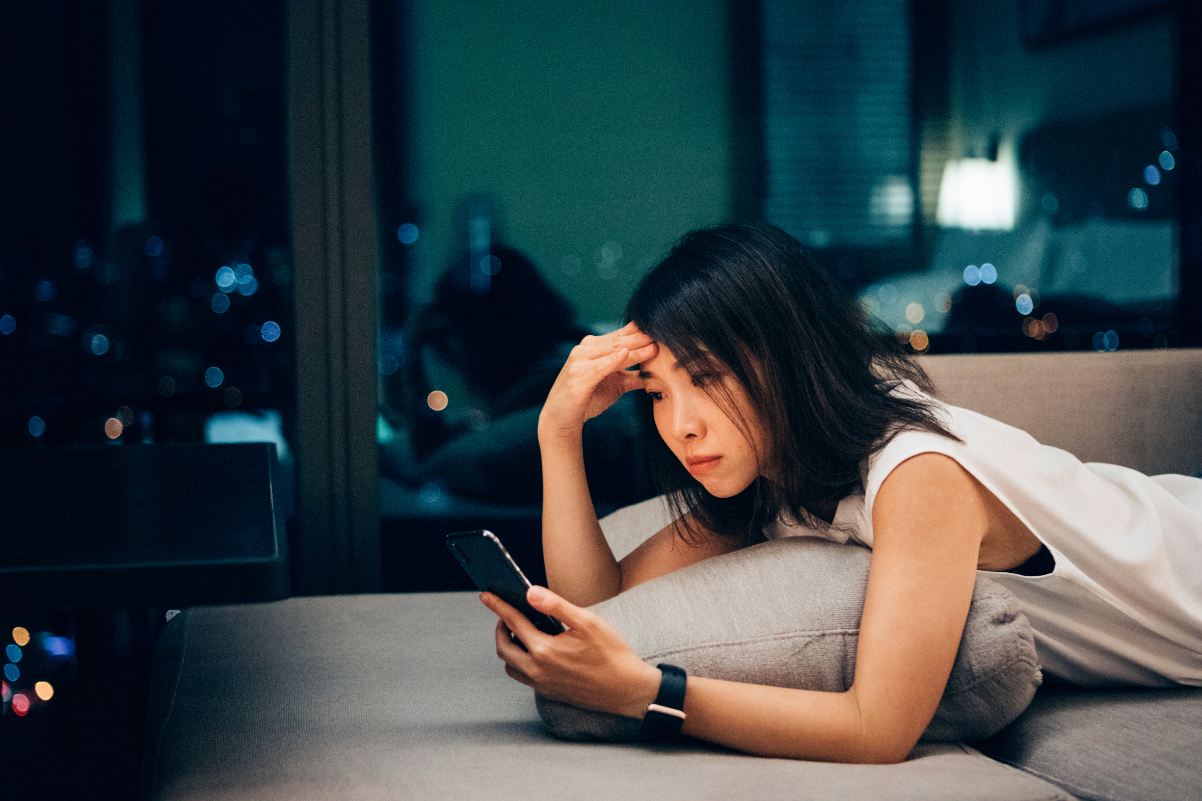 a young woman sits on her phone at home, seeming a bit stressed