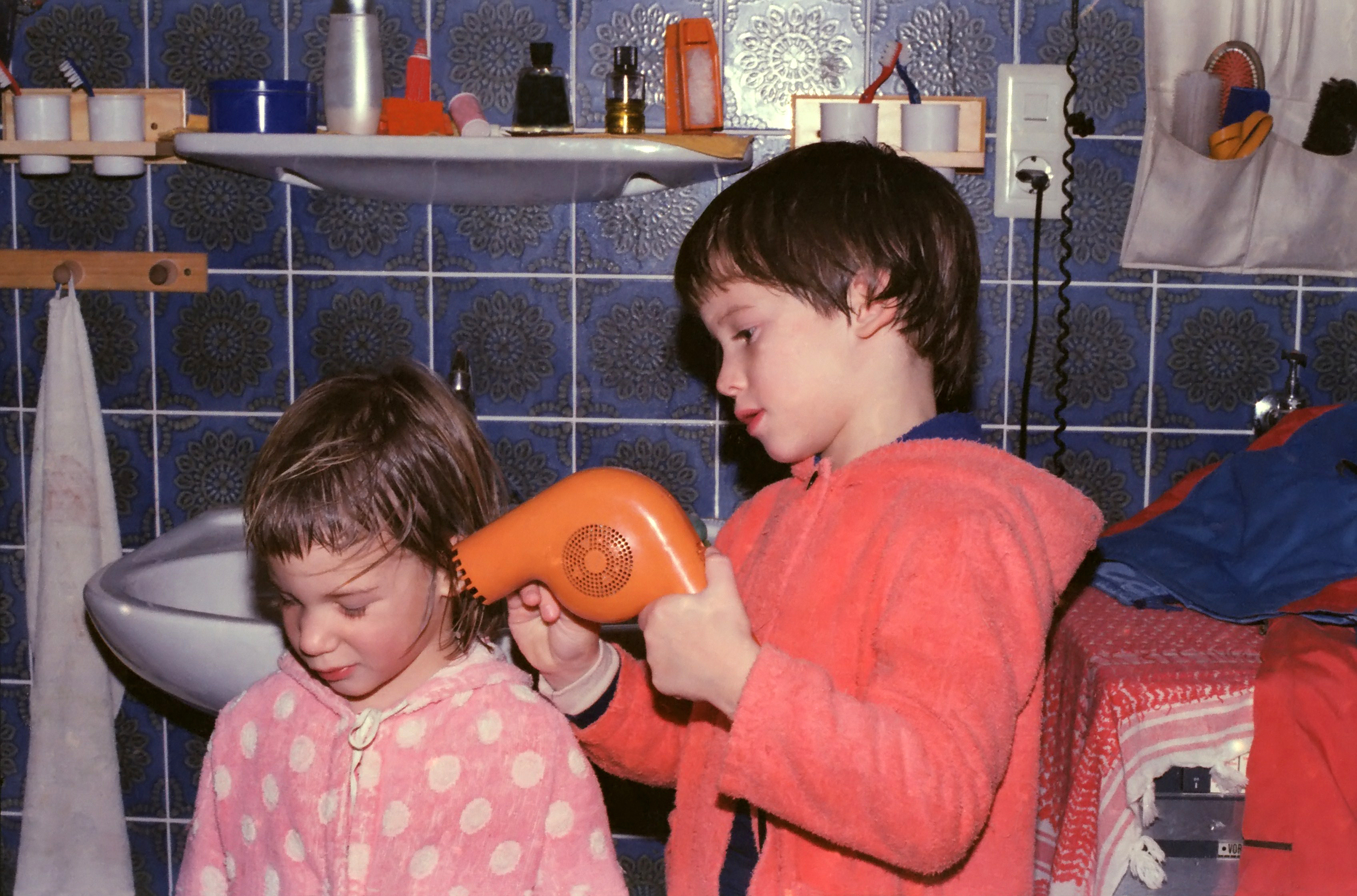A brother is helping her sister blow dry her hair