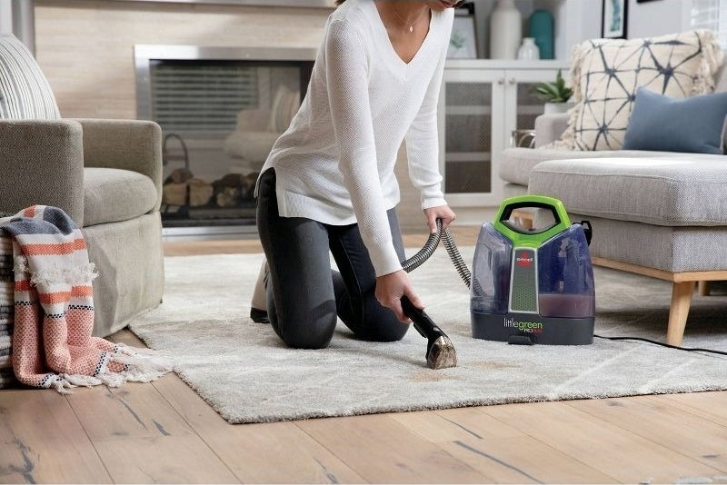 A person cleans a rug with a portable deep cleaning vacuum