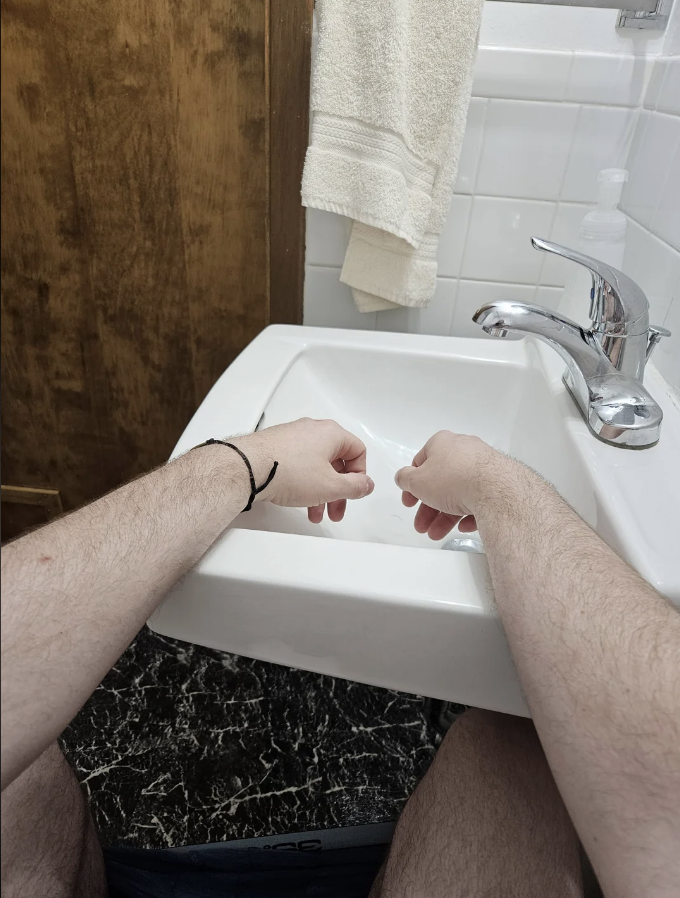 a person on the toilet with their hands draped over the sink