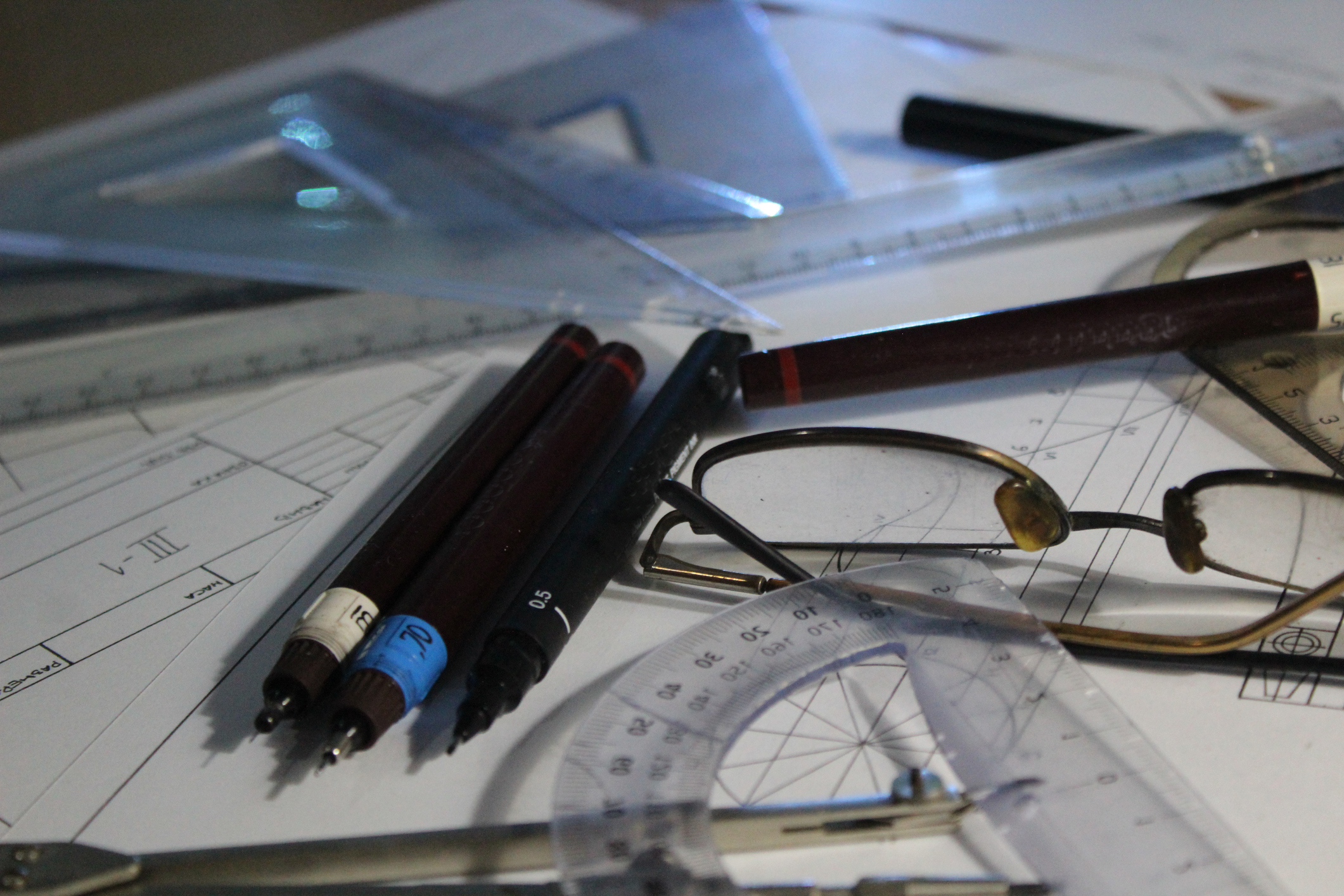 A person&#x27;s desk with glasses, pens, documents