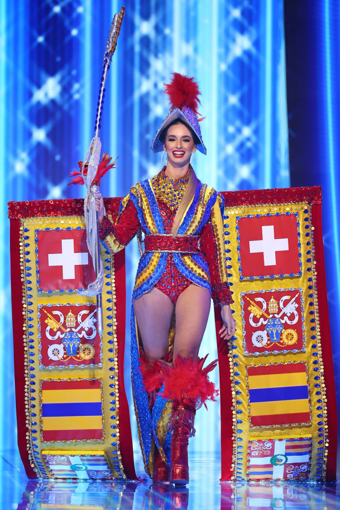 She&#x27;s wearing a very colorful bodysuit, ornate emblem that includes the Swiss flag behind her, and high boots
