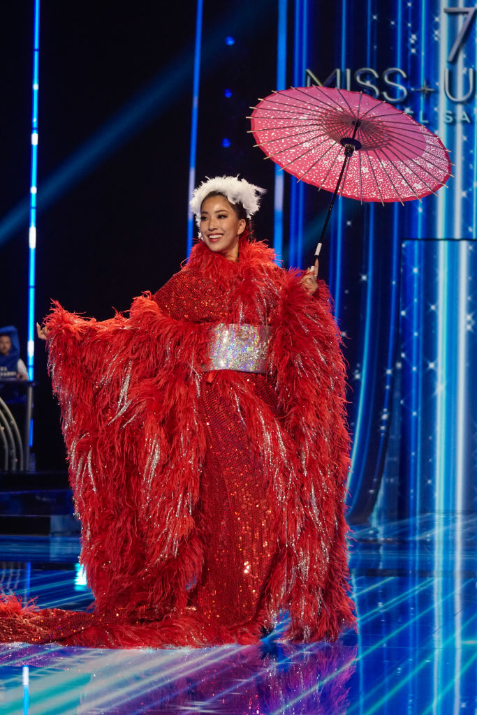 A long, fringed red gown with white accents and paper-bamboo parasol