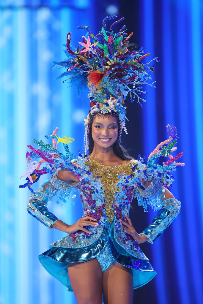 She&#x27;s wearing a colorful, ornate headpiece and matching long-sleeved bodysuit outfit with flared jacket that has an ocean theme