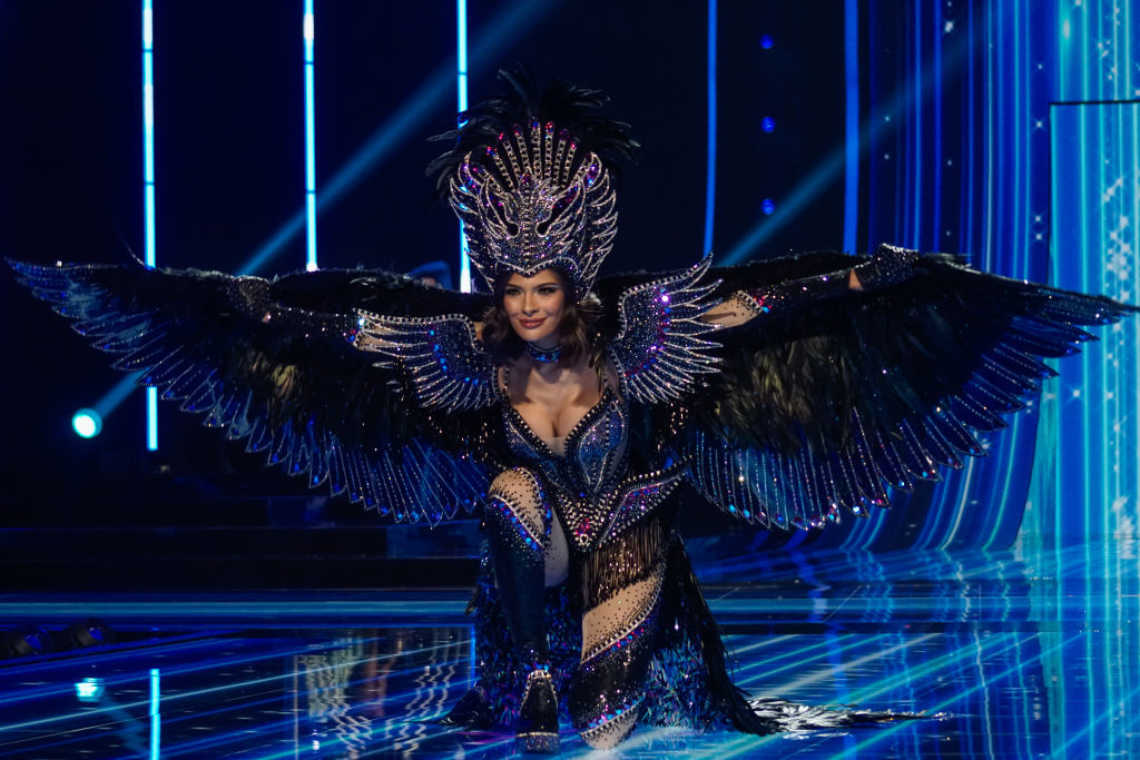 She&#x27;s wearing large headgear and a bejeweled winged outfit