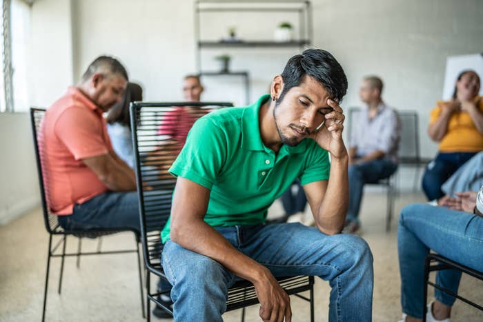 A man sitting and looking pensive as others sit in a group behind him