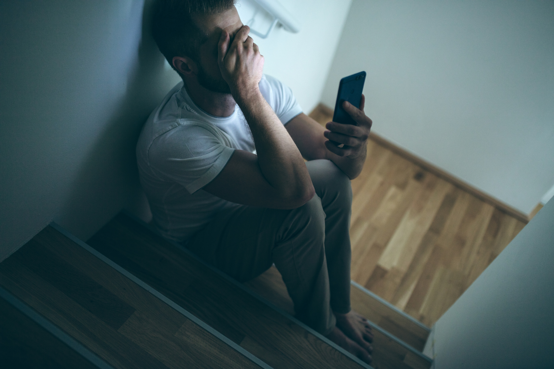 A man with his phone in one hand and his other hand covering his face as he sits on the stairs