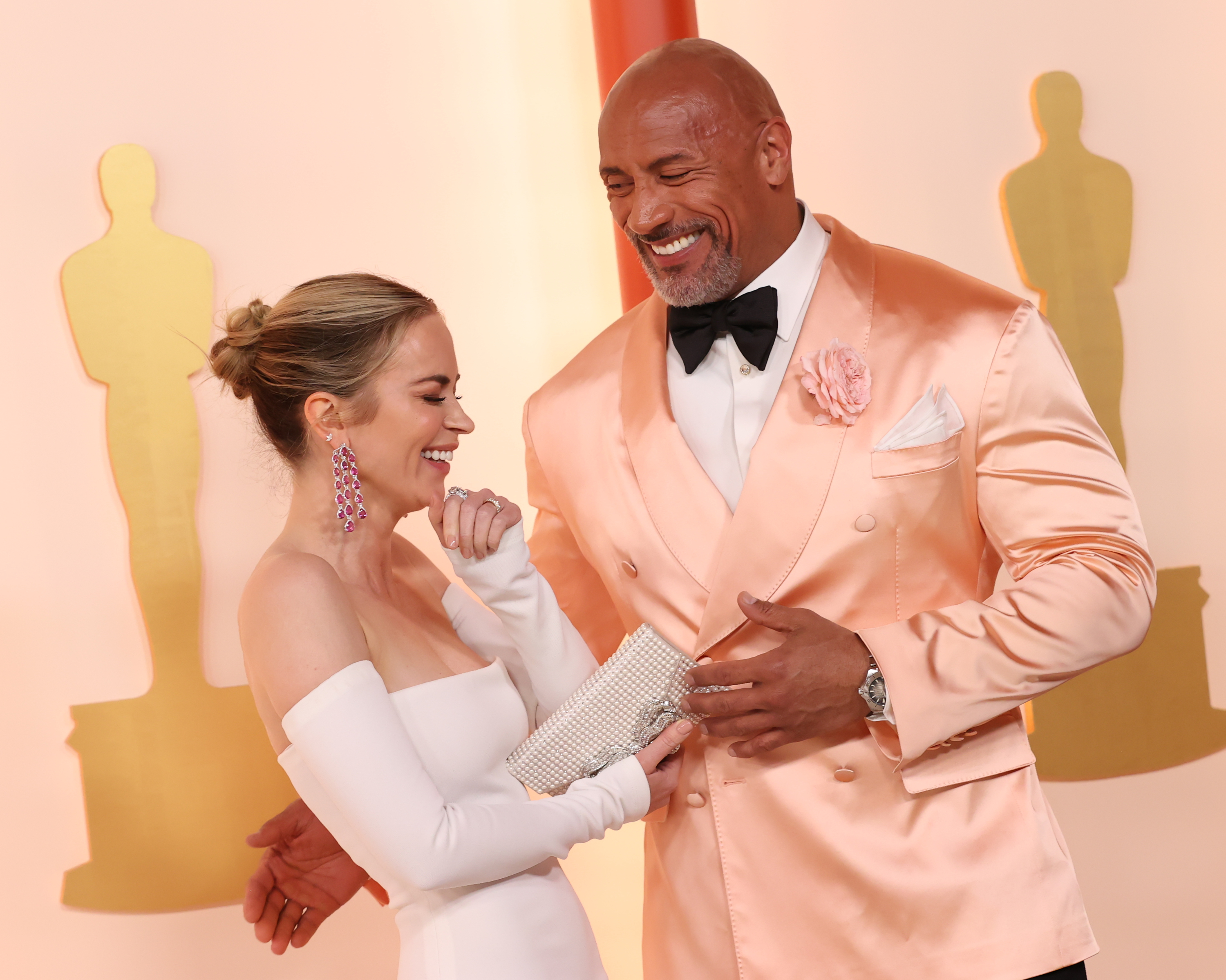 Dwayne in a peach suit while standing next to Emily Blunt on the red carpet at the Oscars