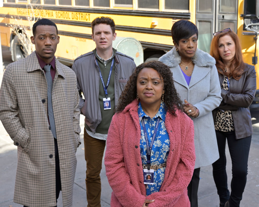Close-up of Quinta with other cast members on the show standing in front of a school bus