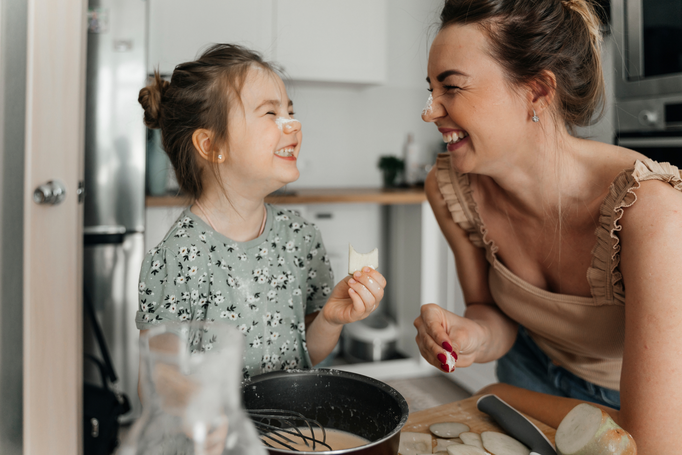 A woman bakes with her daughter; they both have flour on their noses