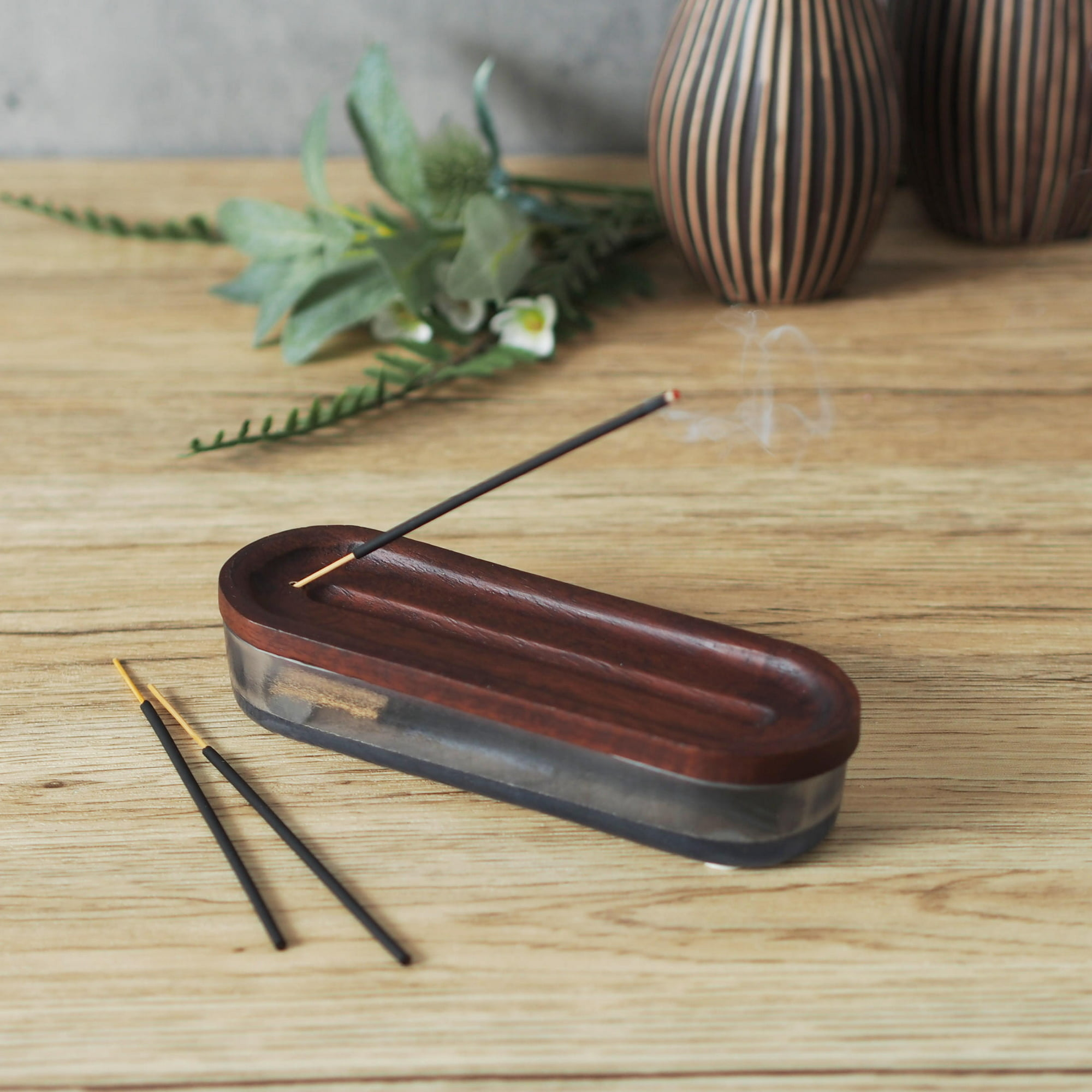 a wooden incense holder and glass container combination with short incense sticks
