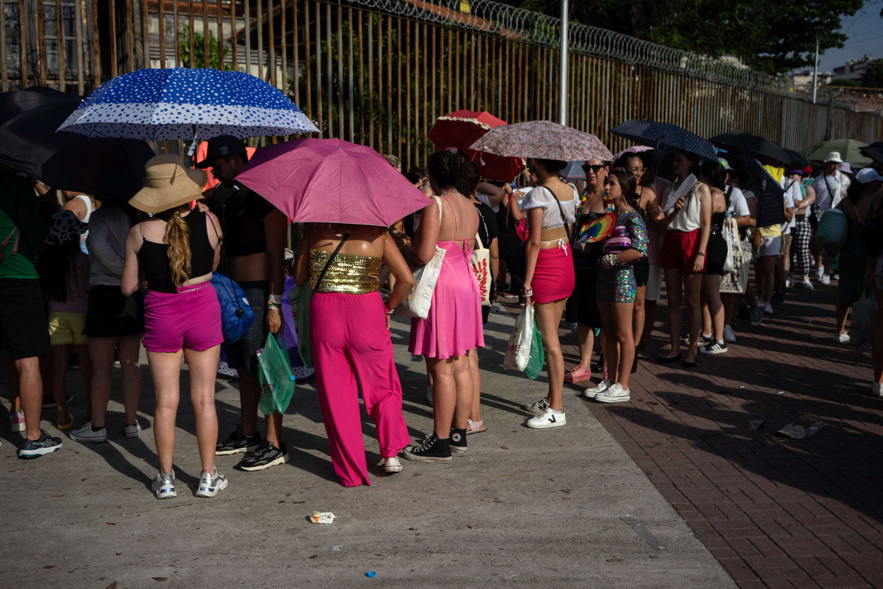 People standing in line, some with sun umbrellas