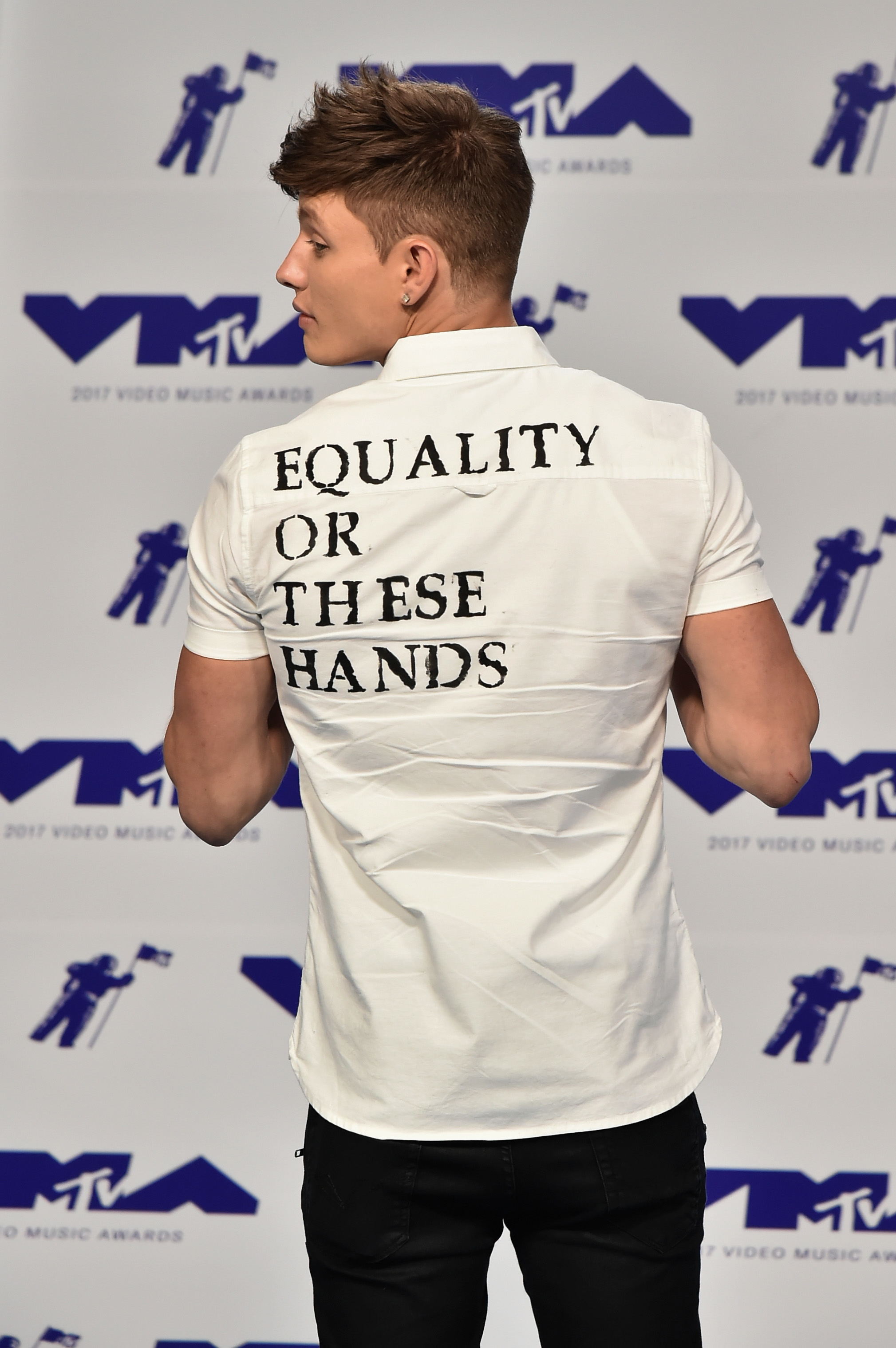 Closeup of Matt Rife showing his back to the camera with a shirt that says &quot;Equality or these hands&quot;