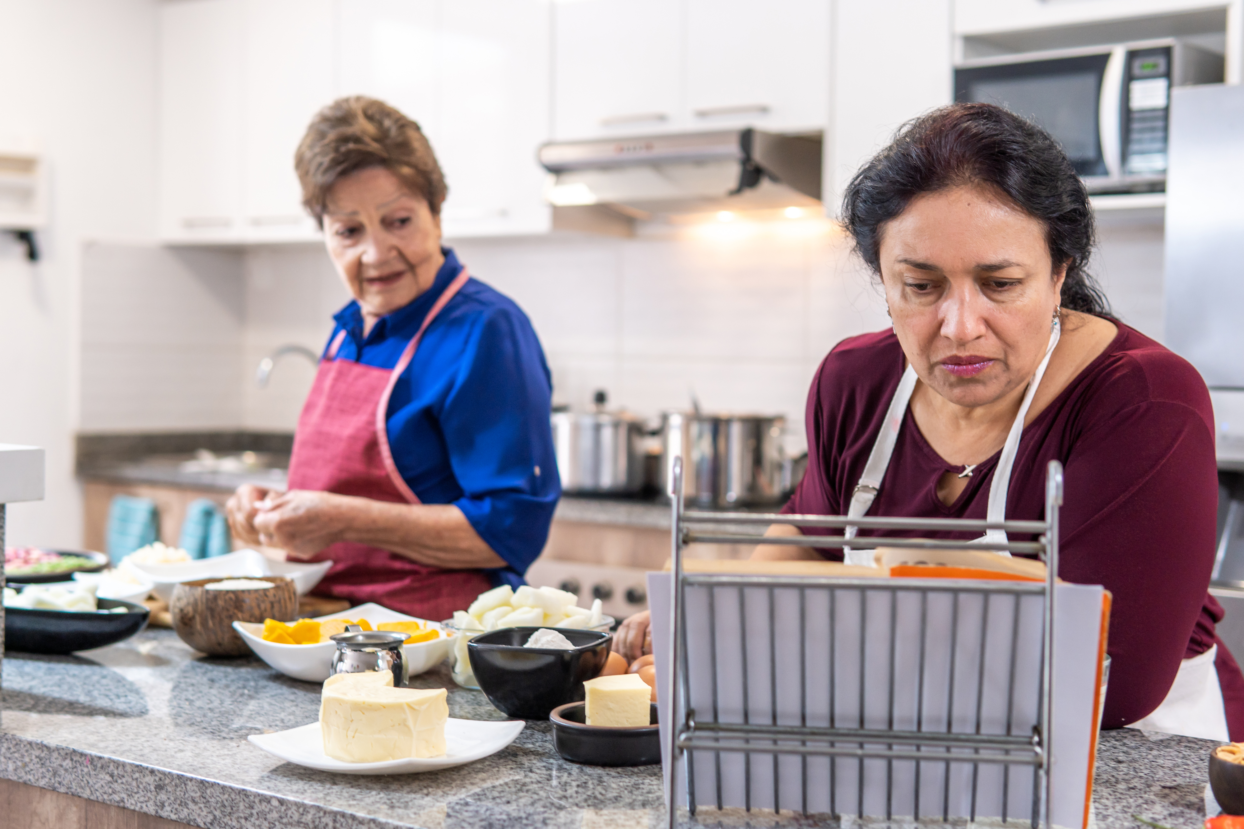 Two older women following a recipe book while they cook