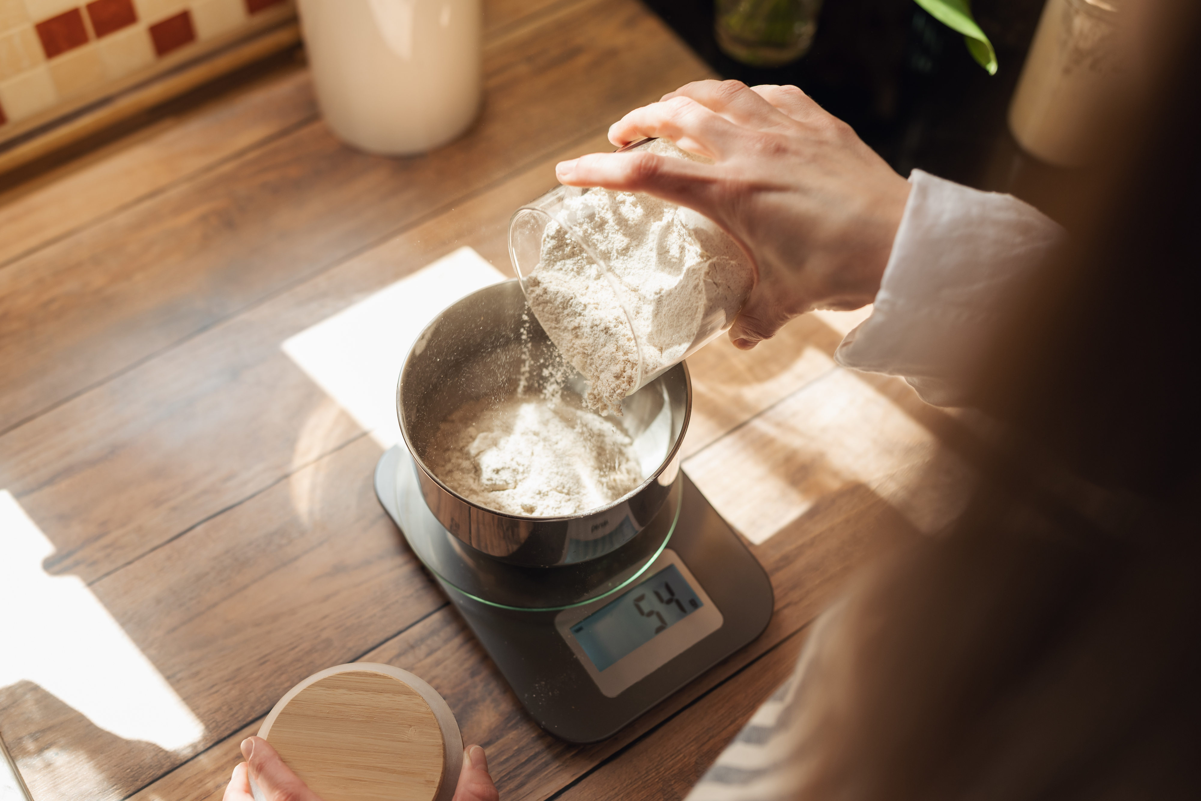 someone pouring flour into a bowl that sits on top of a food scale