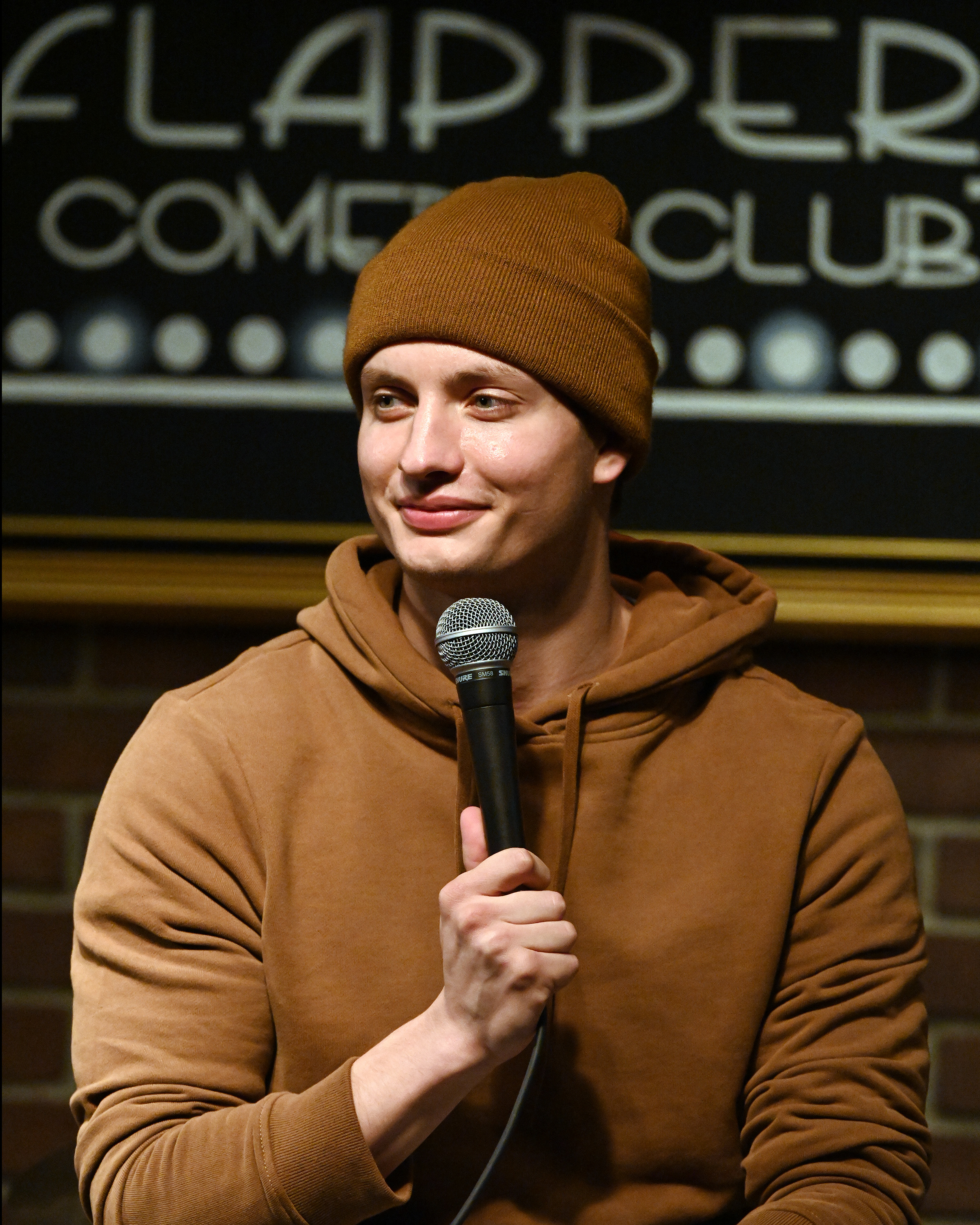 Closeup of Matt Rife in a hoodie and a beanie holding a microphone