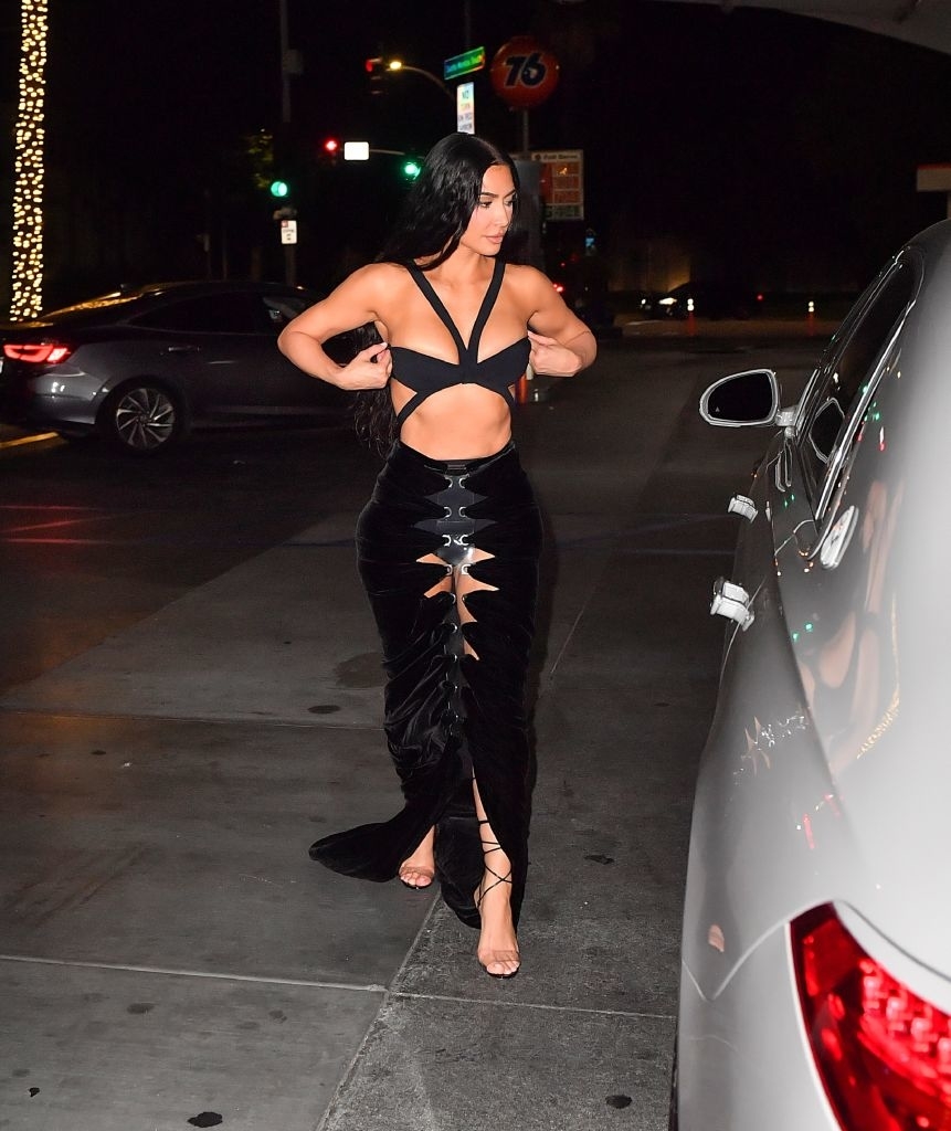 kim walking towards her car wearing a long dress with the midriff cut out as well as cutouts long the center thigh to show her underwear