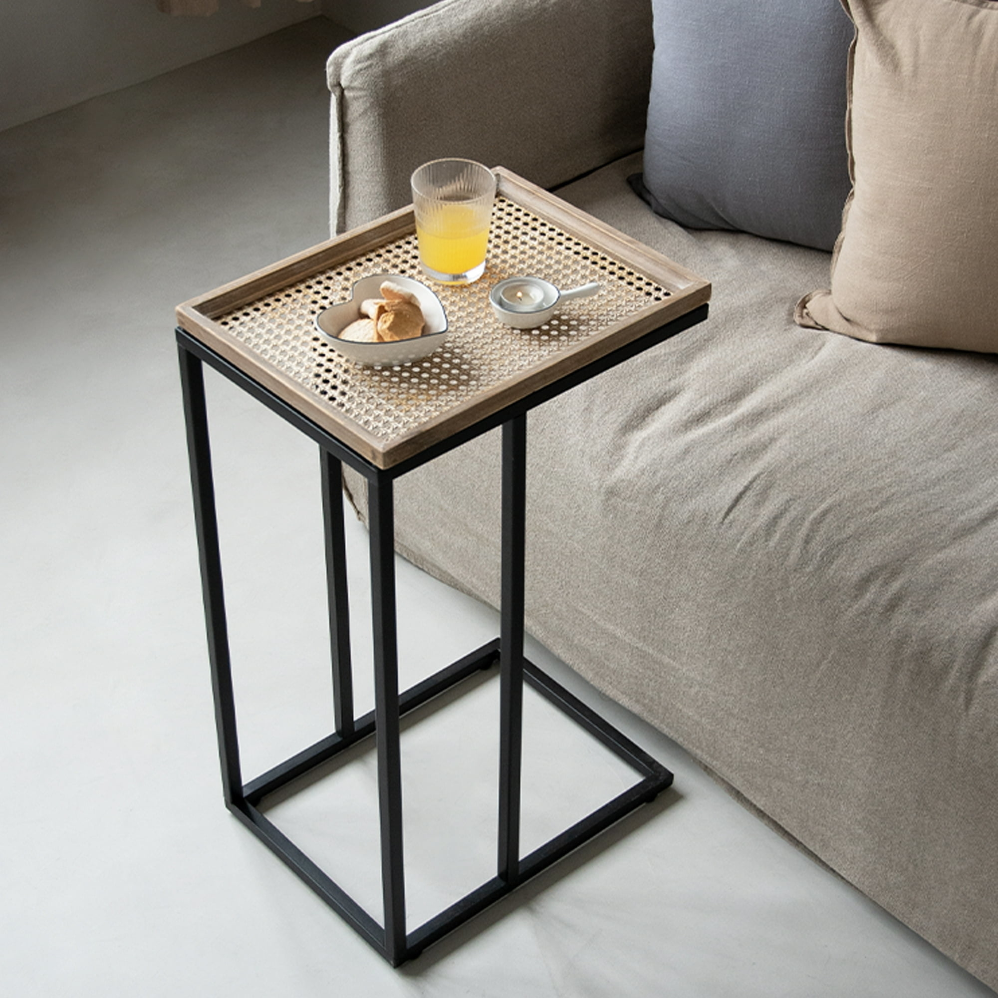 a black and brown end table with a wicker design holding juice and a small bowl of cookies