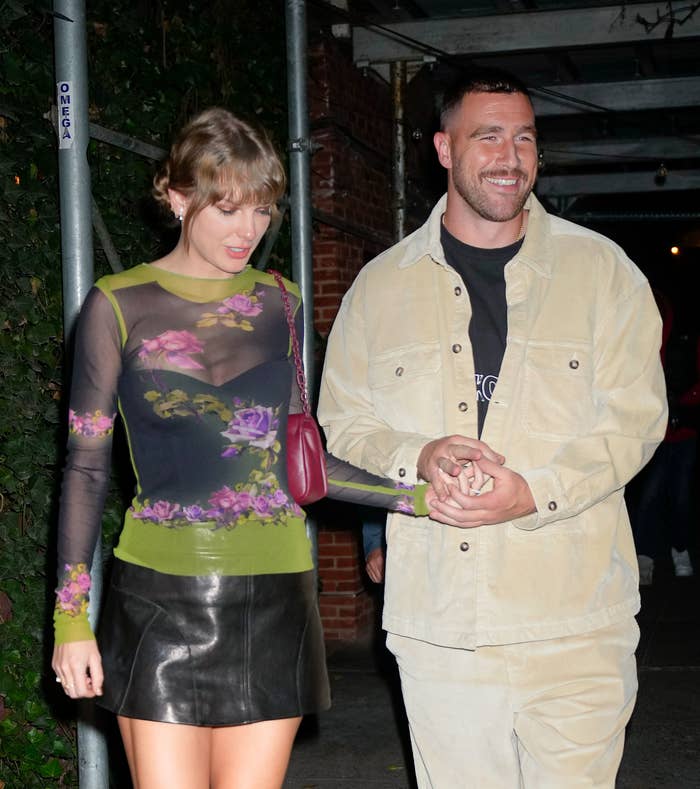 Taylor and Travis holding hands as they walk out of a building
