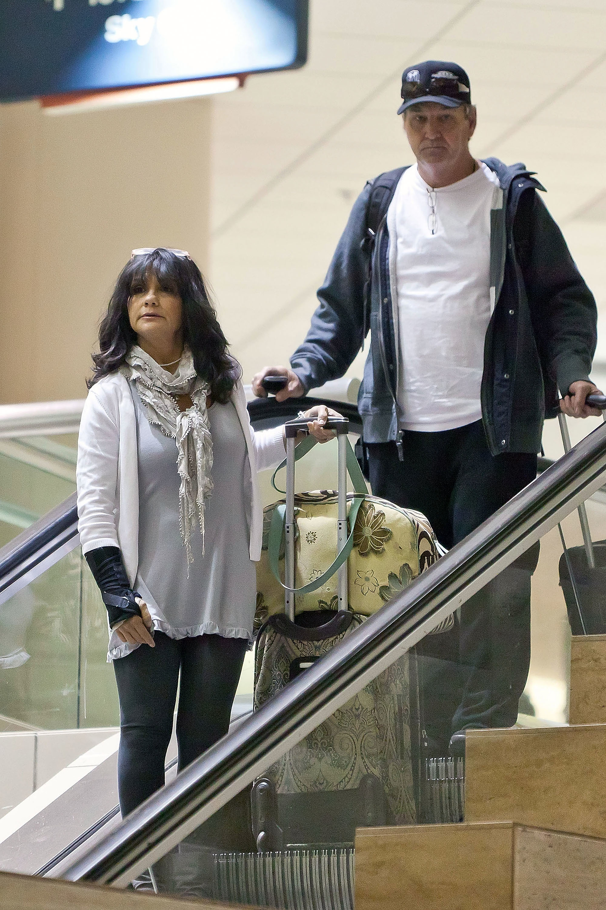 Lynne and Jamie Spears holding luggage and going down an escalator