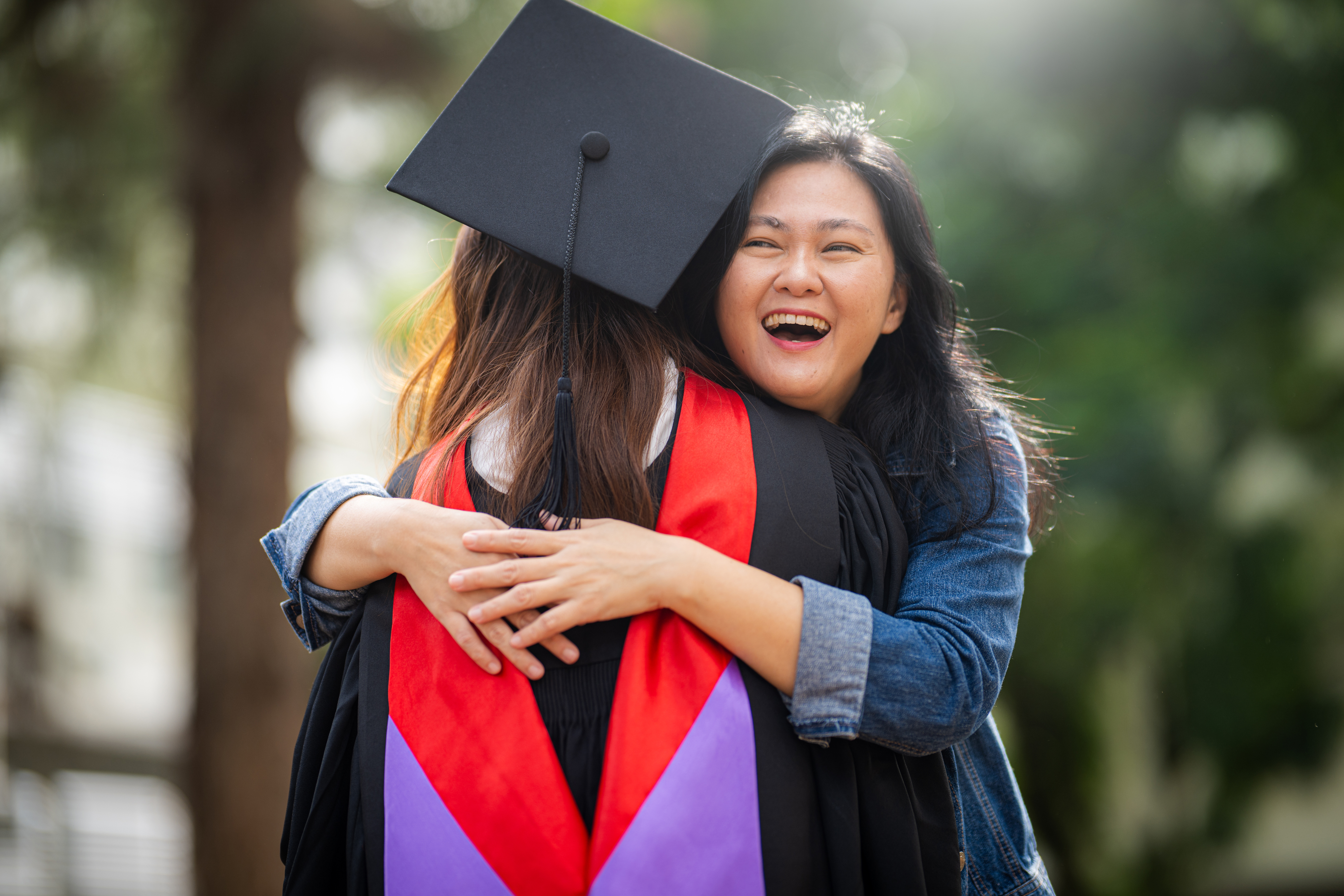 a woman smiling and hugging a college graduate