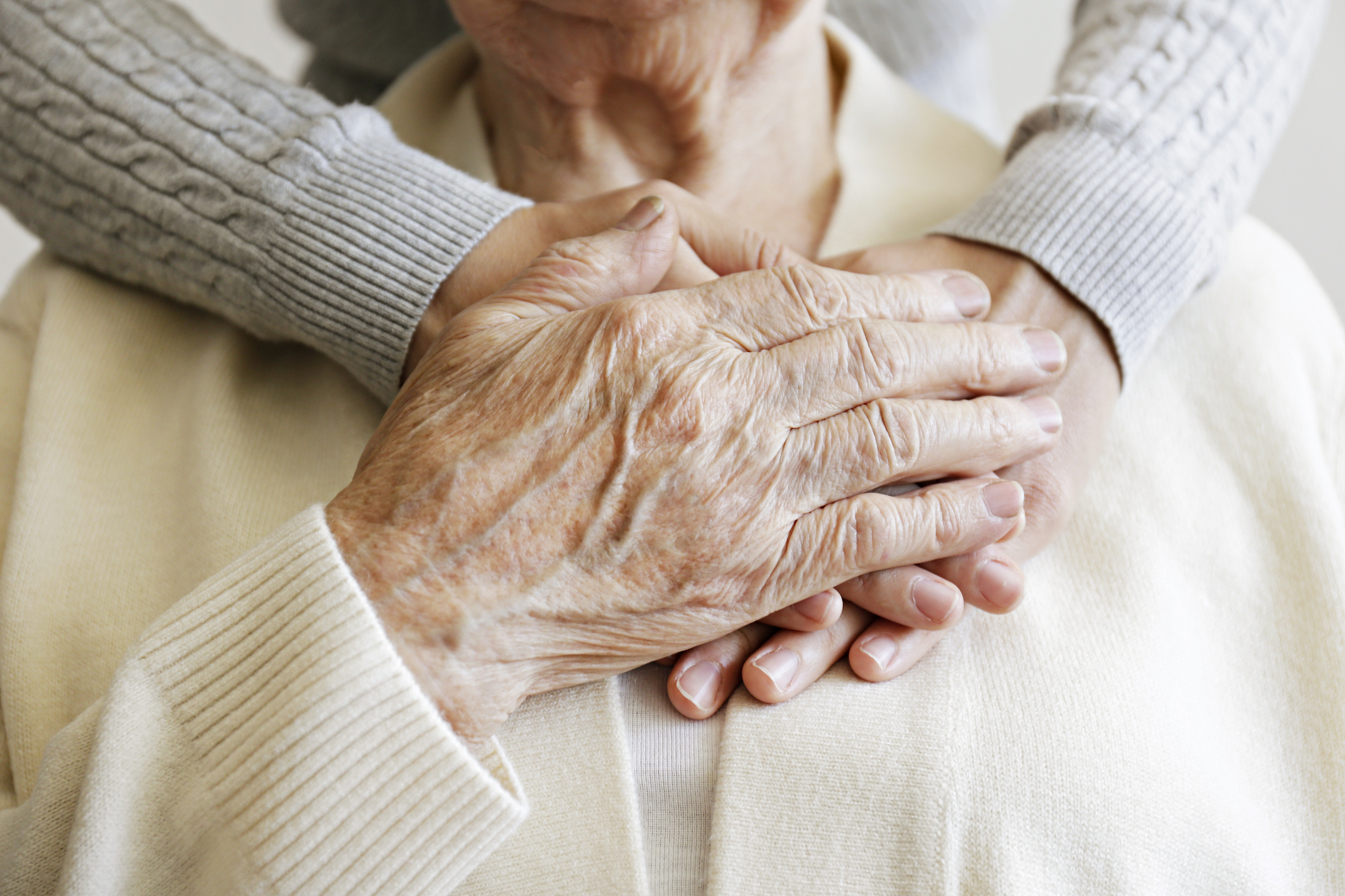 Elderly hands hold a woman&#x27;s hands and arms draped over their shoulder