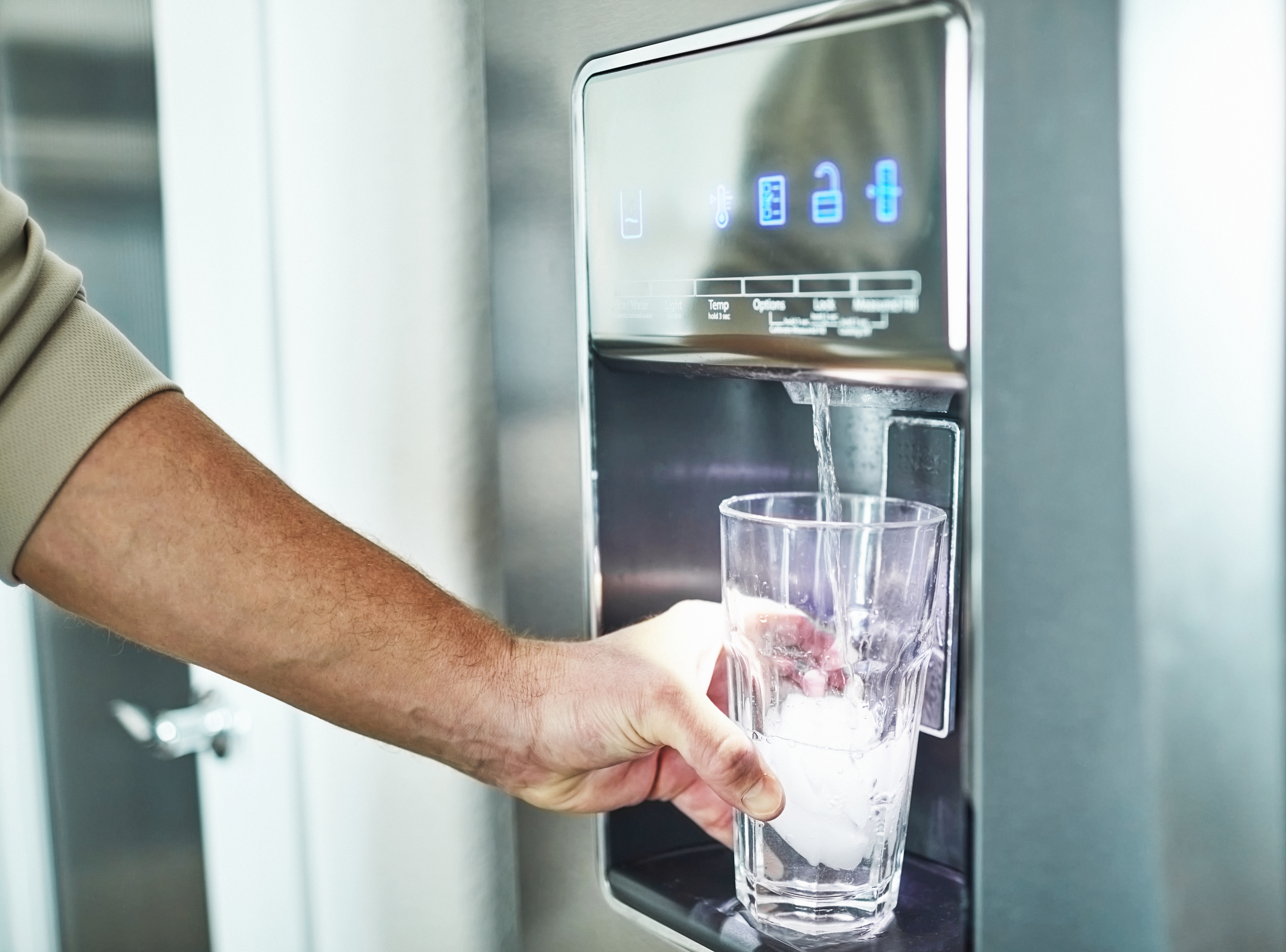 man filling a glass of water from the refrigerator dispenser