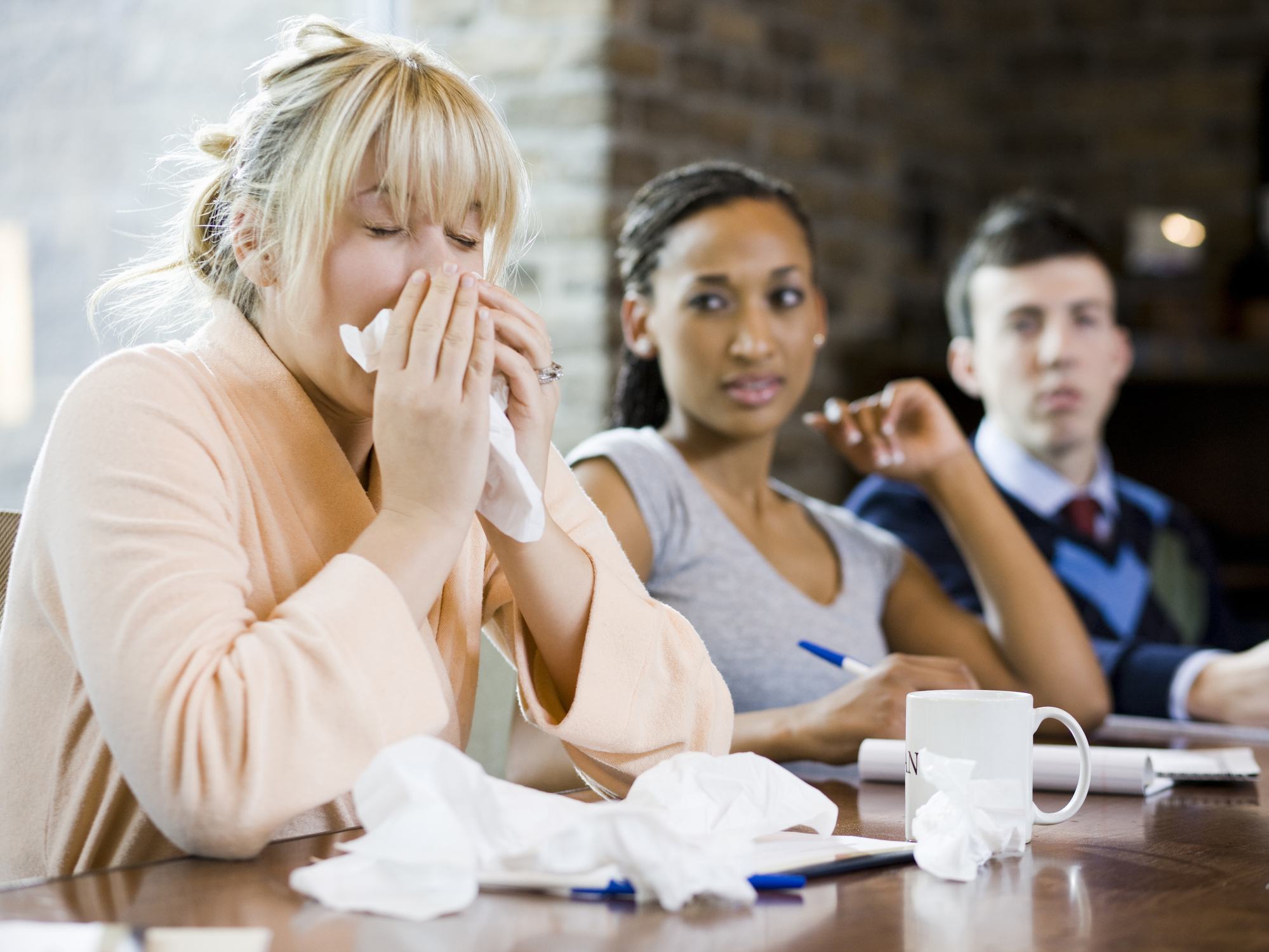 A person sneezing and blowing their nose in a conference room