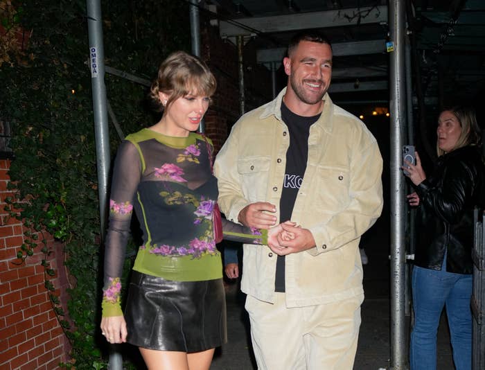 Closeup of Taylor Swift and Travis Kelce holding hands as they exit a building at night