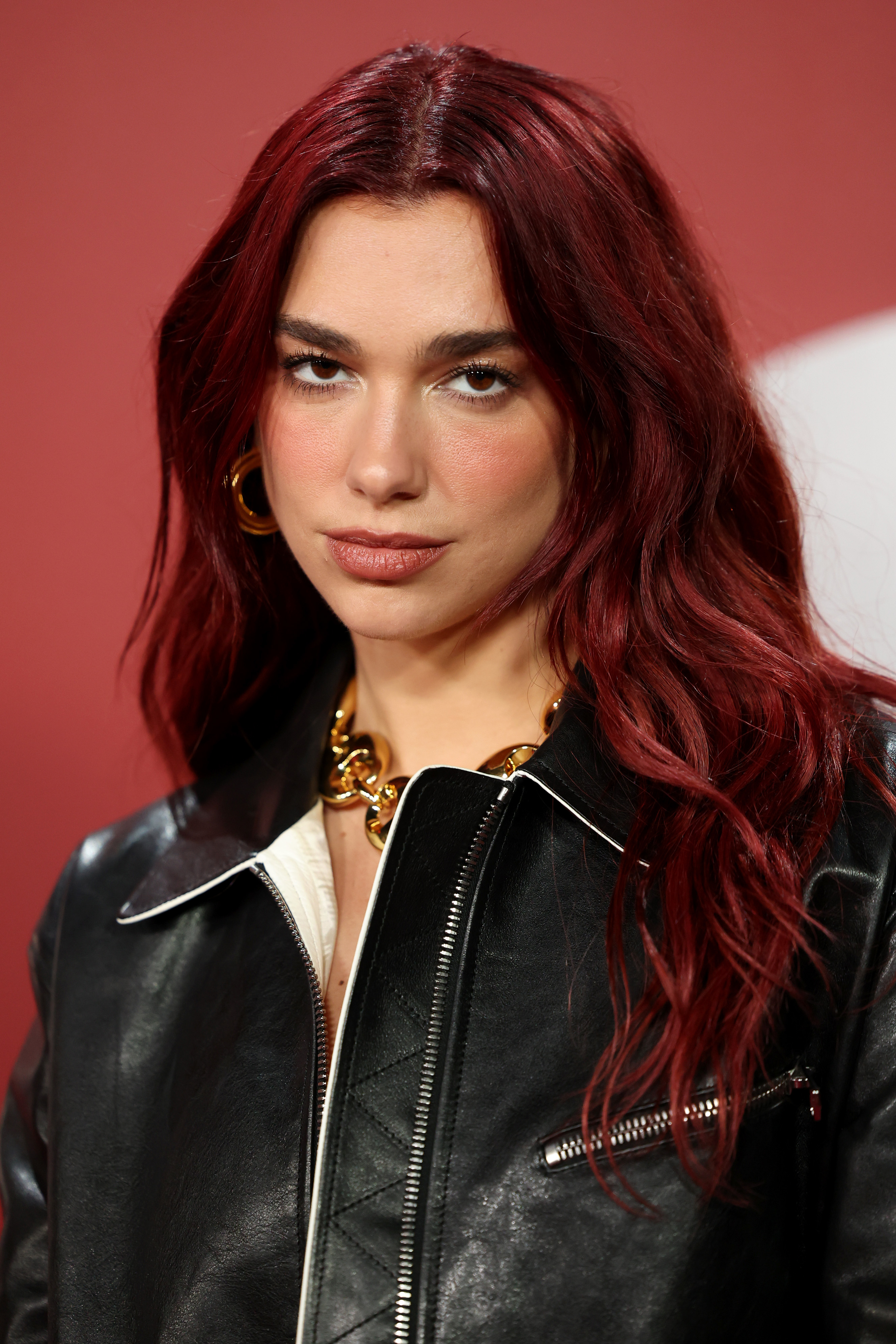 Dua Lipa looks at the camera wearing a leather jacket and chunky gold necklace.