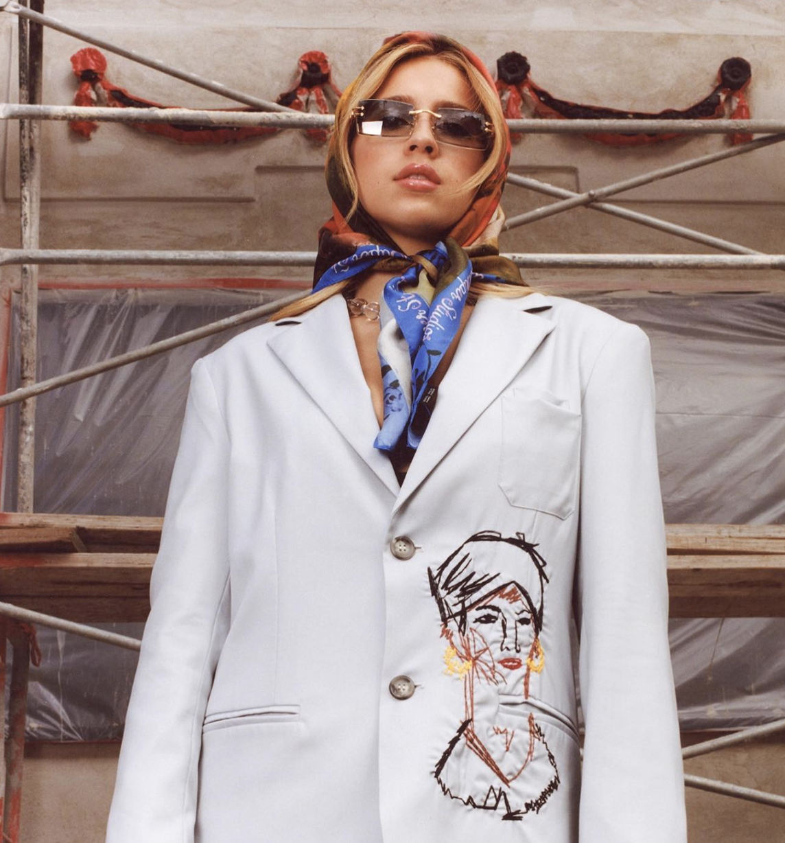 Tate McRae poses in an oversized white jacket, a silk head scarf and sunglasses.