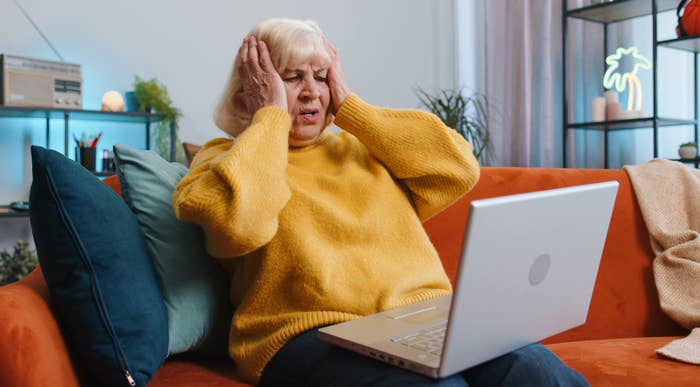 A woman with her hands on her head while sitting in front of a laptop