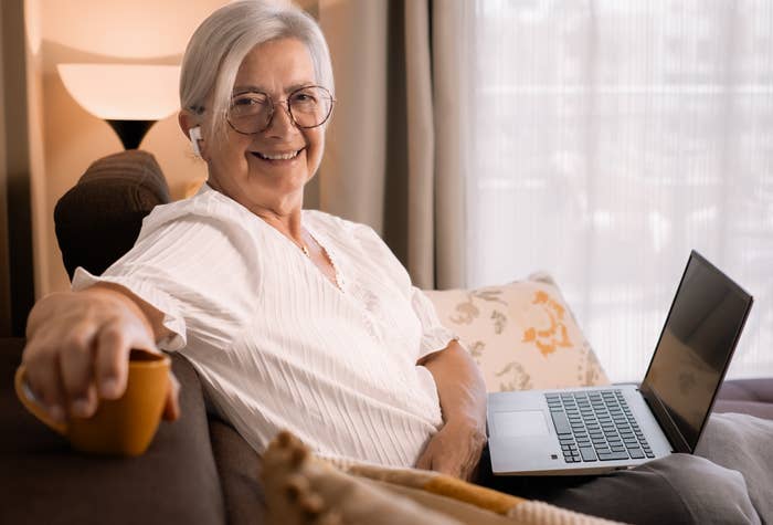 A woman smiling while holding a cup of coffee in front of her laptop