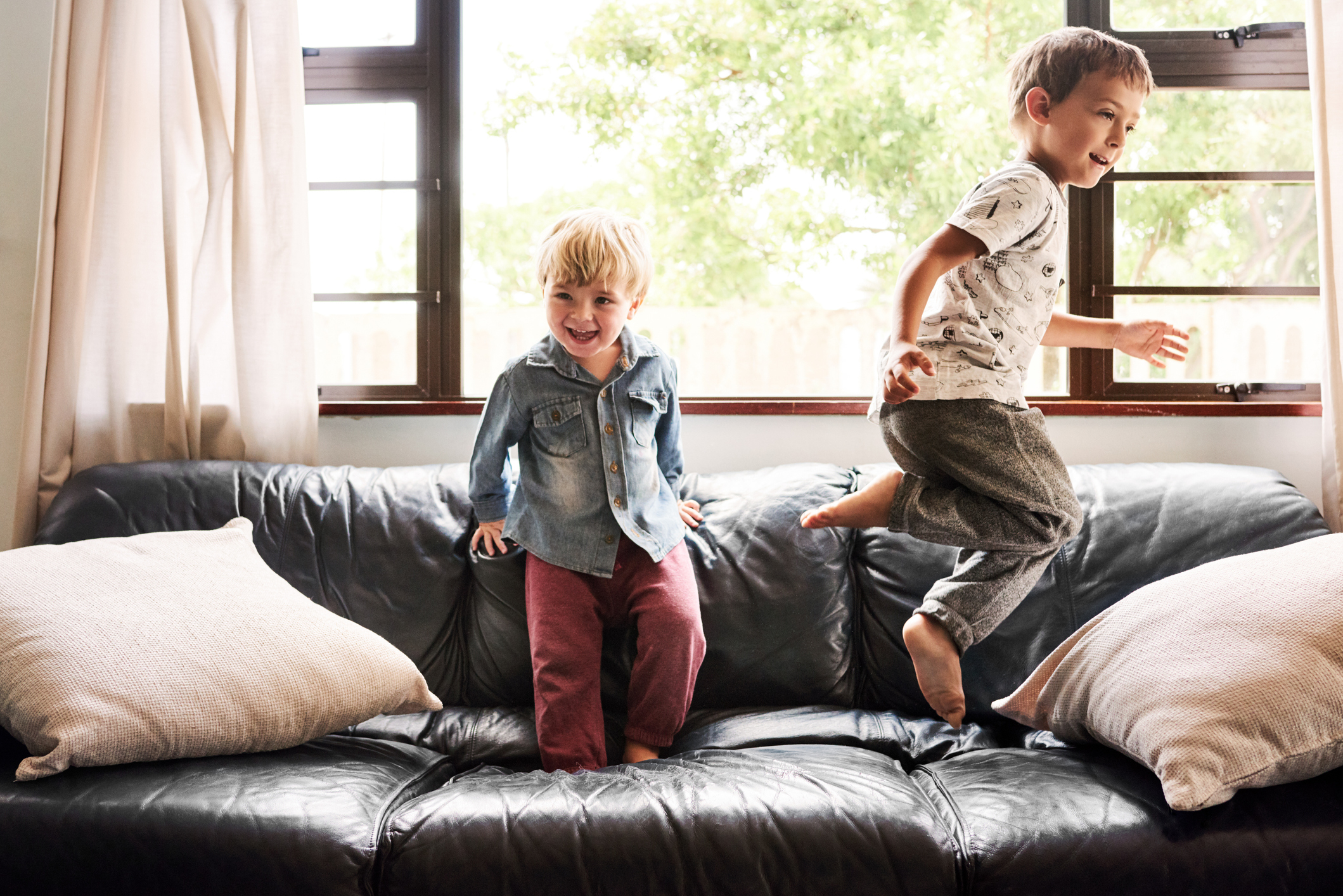 Two young boys are jumping on a couch